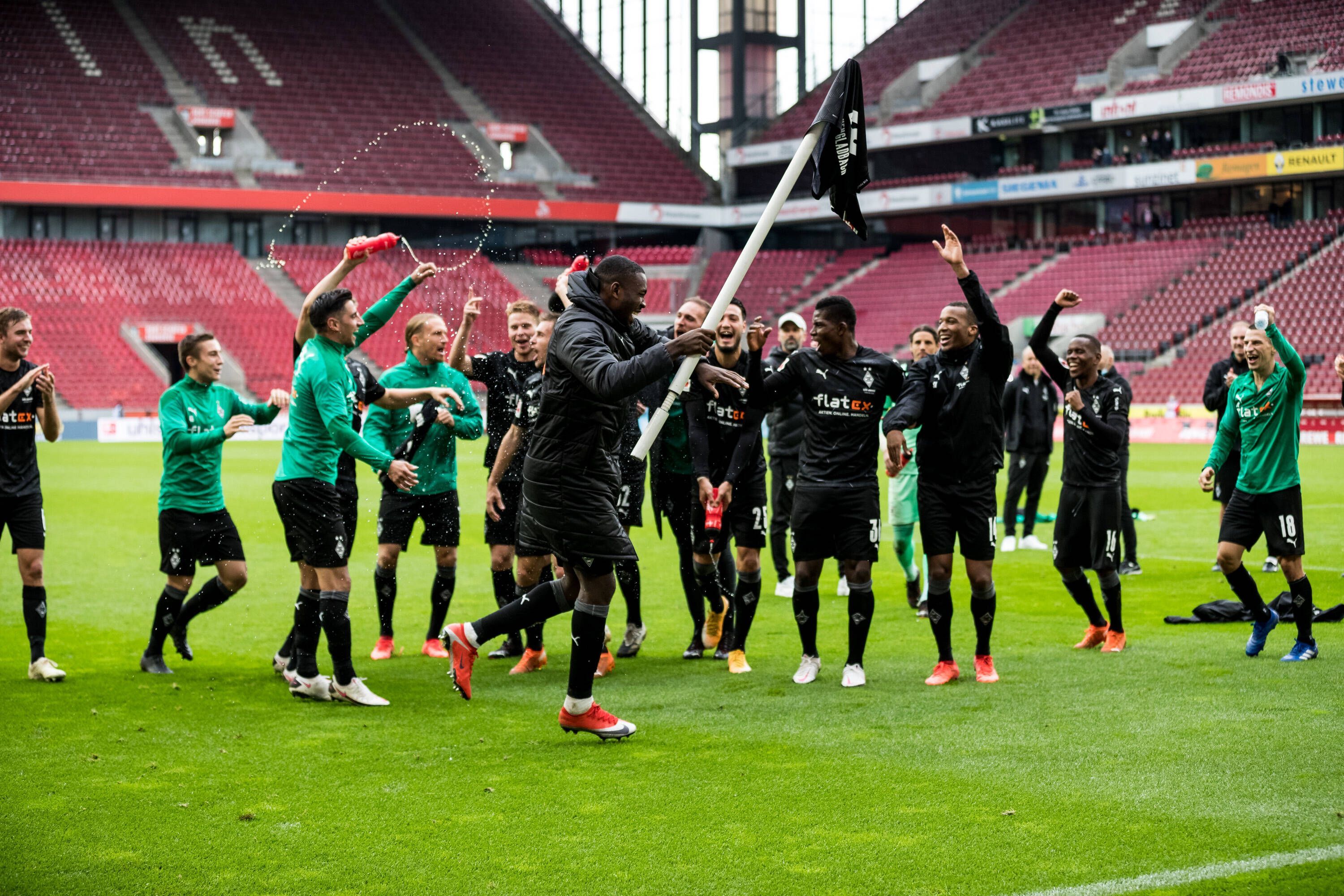 Gladbachs Marcus Thuram jubelt in Köln mit einer Eckfahne in der Hand, derweil feuern in seine Team-Kollegen an.