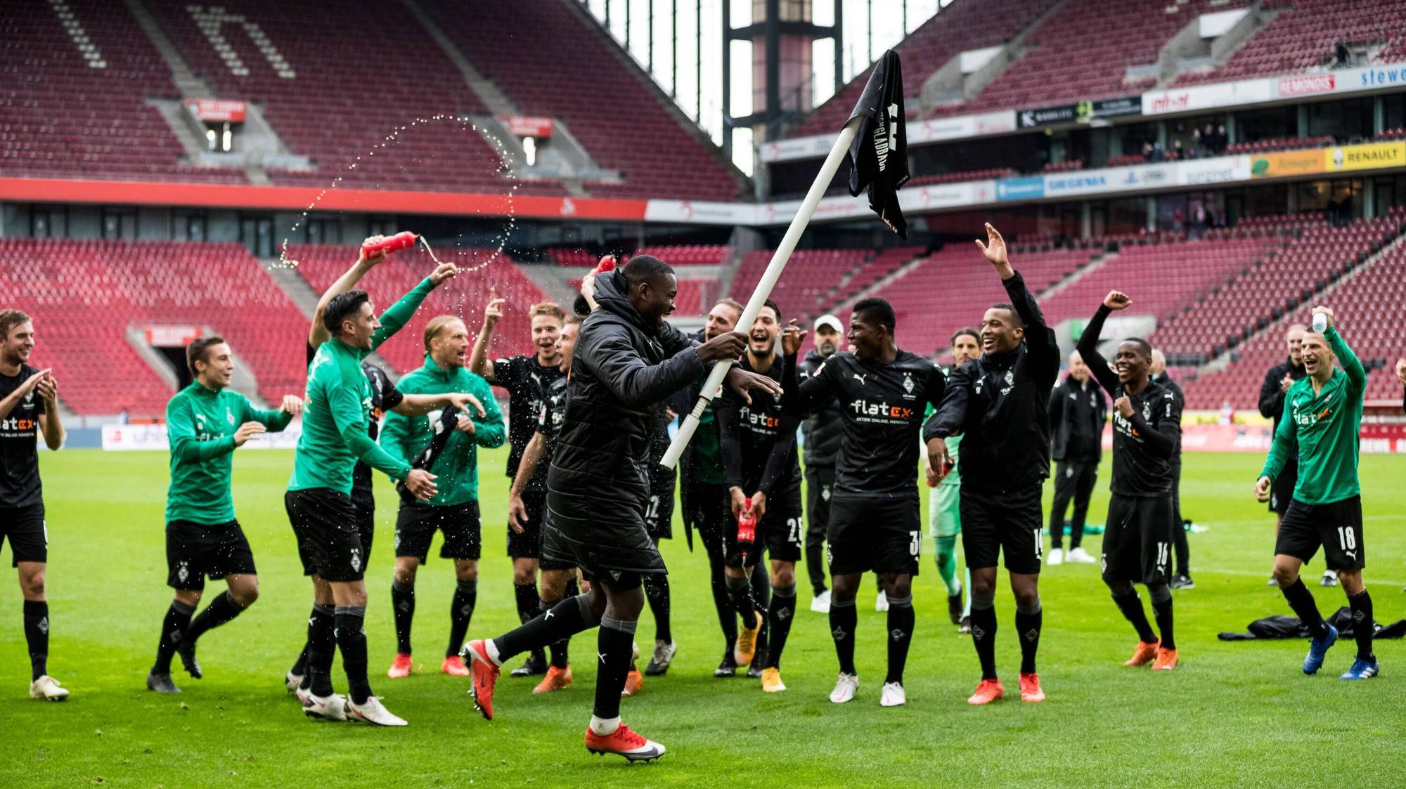 Gladbachs Marcus Thuram jubelt in Köln mit einer Eckfahne in der Hand, derweil feuern in seine Team-Kollegen an.