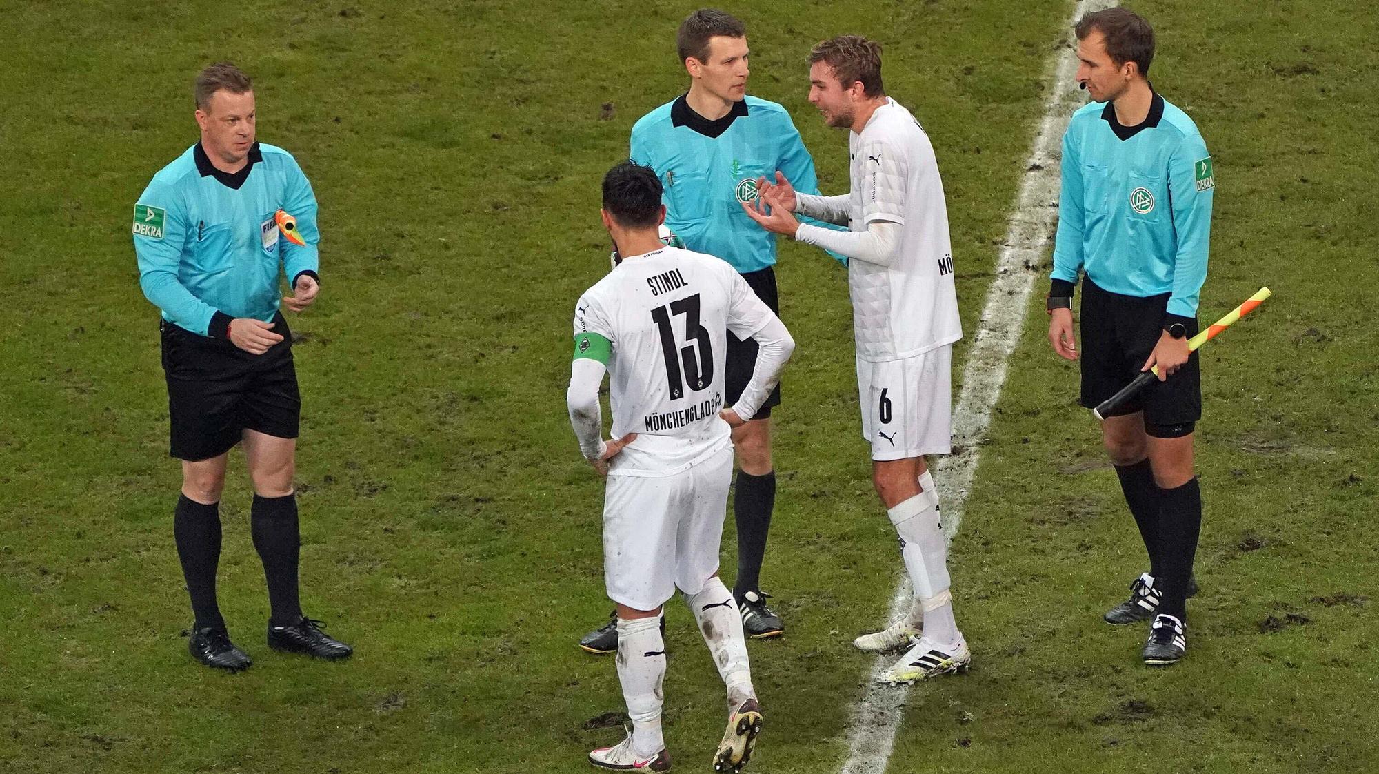 Die Gladbacher Spieler Lars Stindl (mit dem Rücken zur Kamera) und Christoph Kramer (2.v.r.) diskutieren zur Halbzeit mit Schiedsrichter Benjamin Cortus (Mitte).