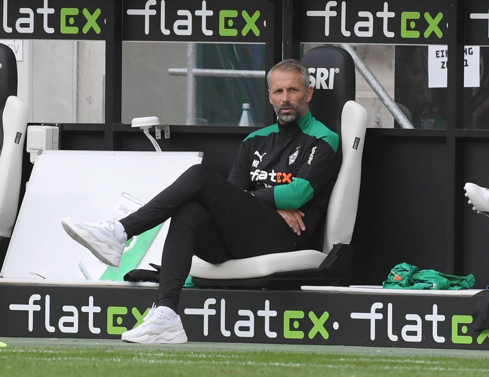 Marco Rose, Fußballlehrer in Diensten von Fußball-Bundesligist Borussia Mönchengladbach, sitzt auf der Trainerbank im Borussia und schaut von dort dem Spielgeschehen auf dem Platz zu.