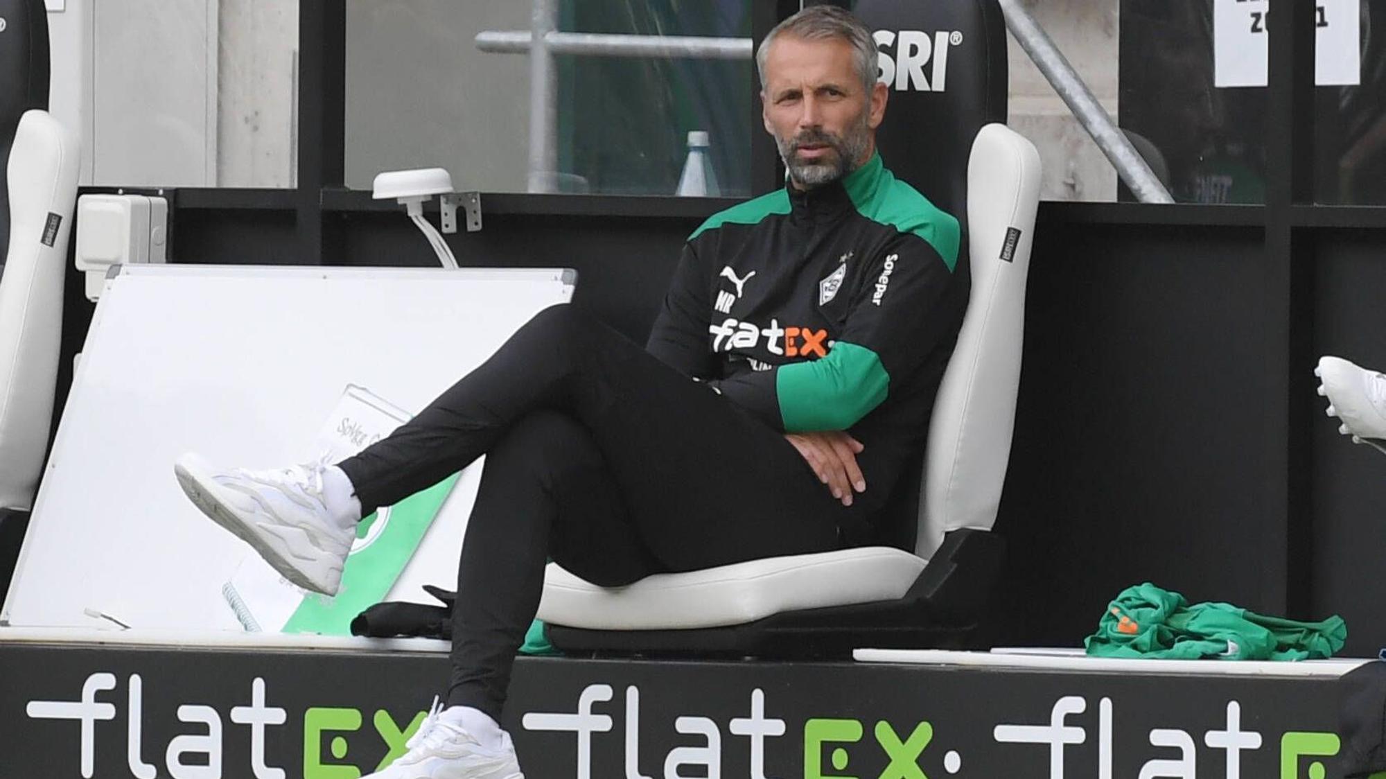 Marco Rose, Fußballlehrer in Diensten von Fußball-Bundesligist Borussia Mönchengladbach, sitzt auf der Trainerbank im Borussia und schaut von dort dem Spielgeschehen auf dem Platz zu.
