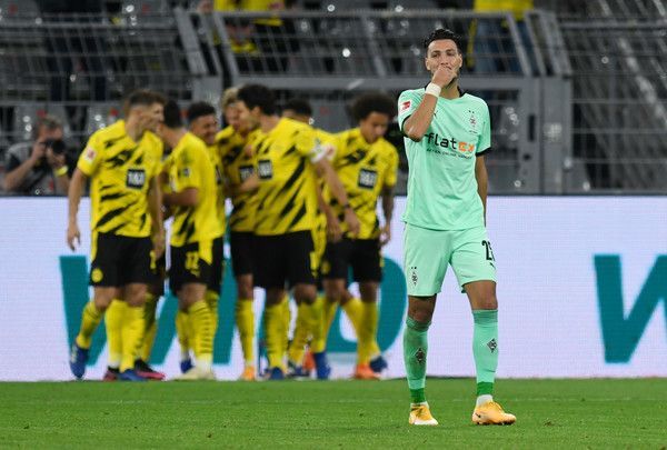 Gladbachs Fußballer Ramy Bensebaini greift sich enttäuscht ins Gesicht. Im Hintergrund jubeln Dortmunder.