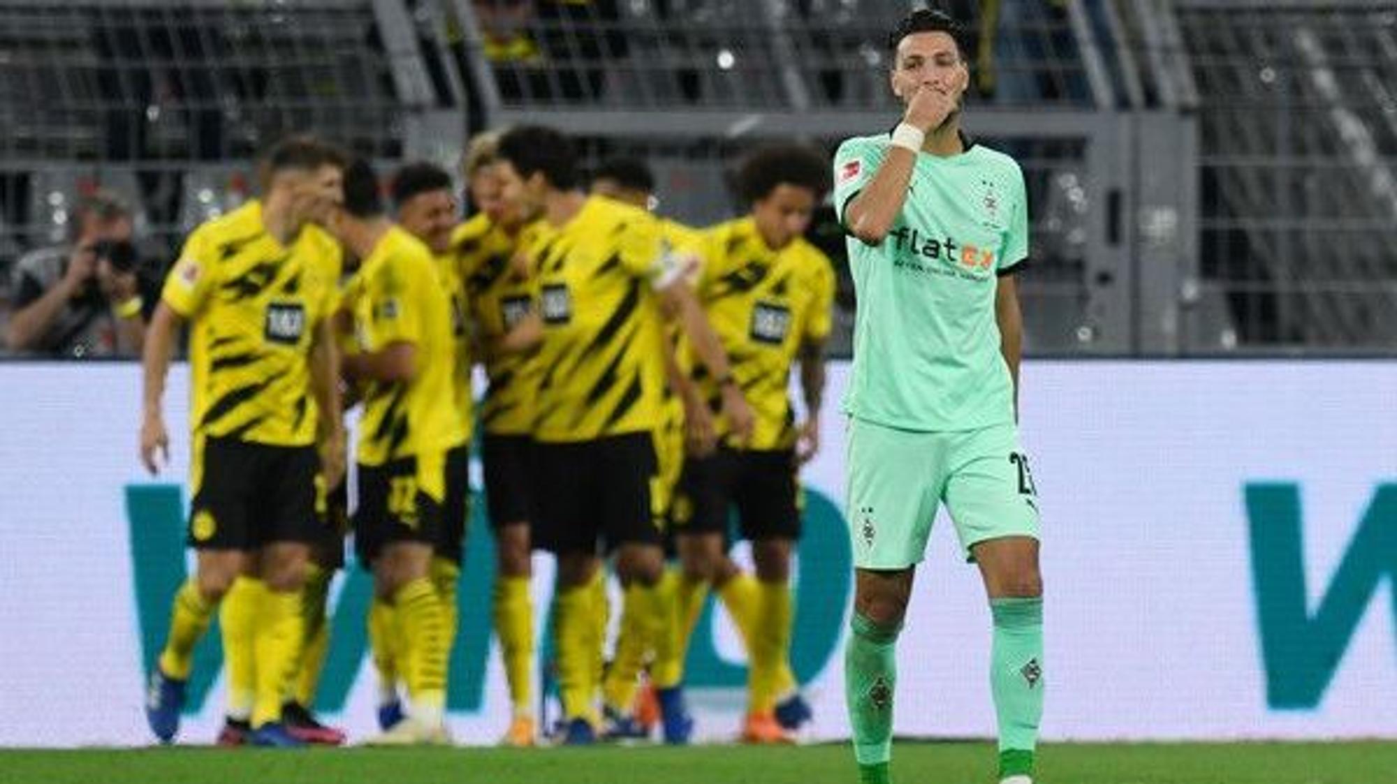 Gladbachs Fußballer Ramy Bensebaini greift sich enttäuscht ins Gesicht. Im Hintergrund jubeln Dortmunder.