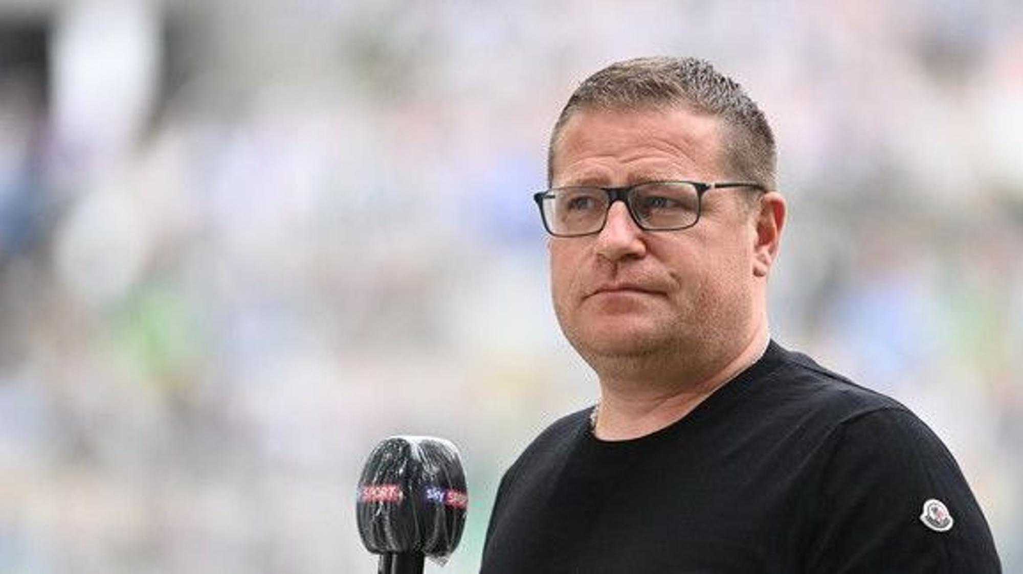 Max Eberl blickt in die Kamera, während ein Mikrofon im entgegengehalten wird.