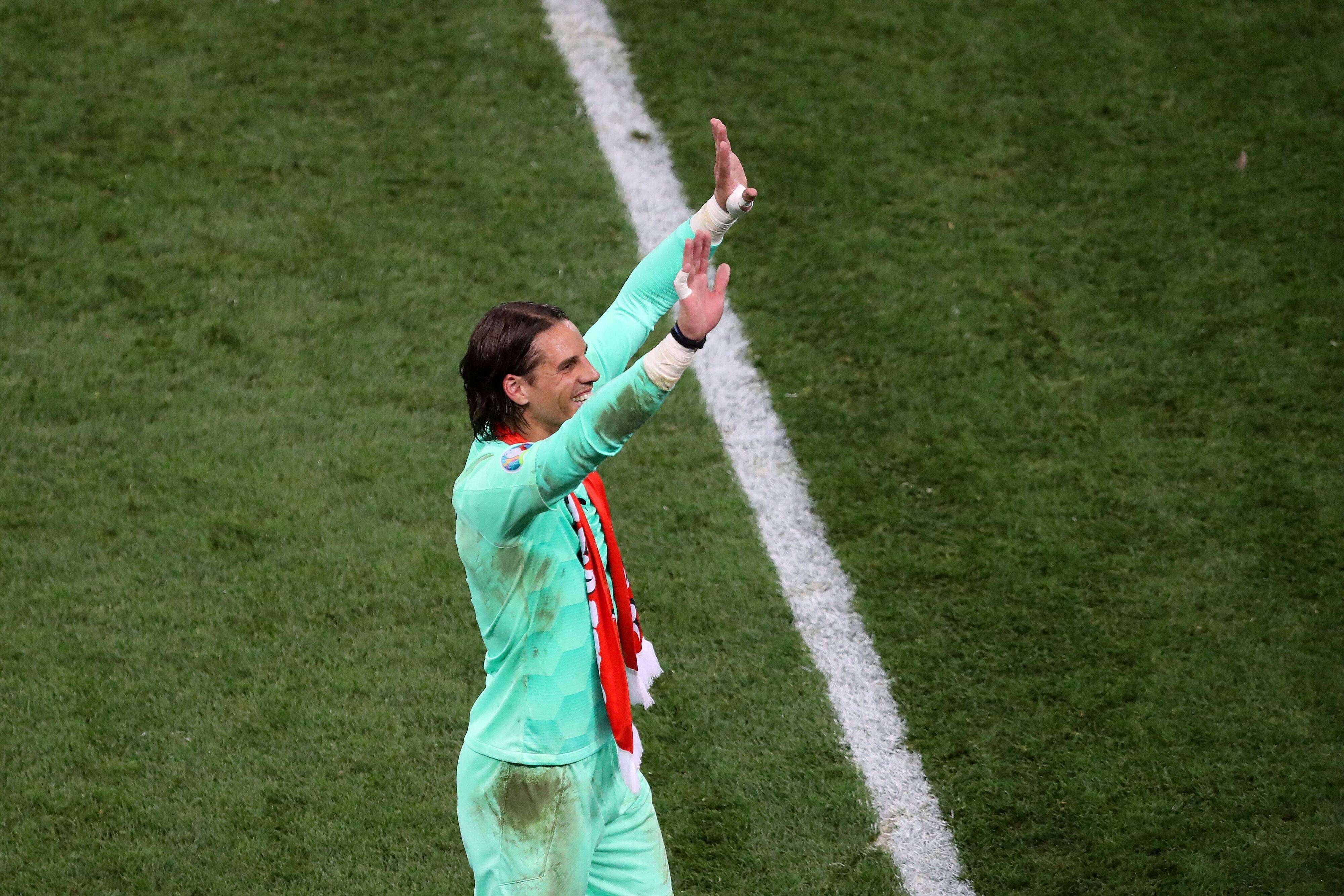 Yann Sommer trägt ein verschmutztes Trikot und hat einen Fan-Schal um den Hals hängen. Seine Arme streckt er in de Himmel und winkt Fans auf der Tribüne zu.