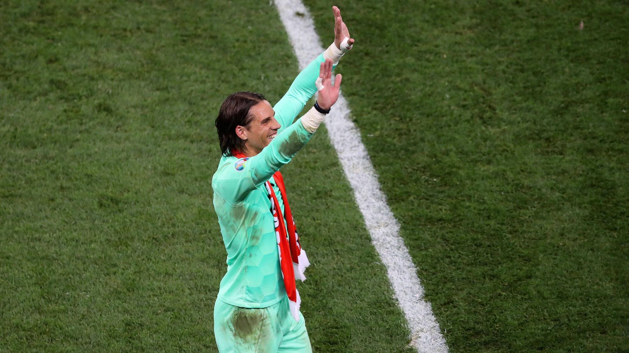 Yann Sommer trägt ein verschmutztes Trikot und hat einen Fan-Schal um den Hals hängen. Seine Arme streckt er in de Himmel und winkt Fans auf der Tribüne zu.