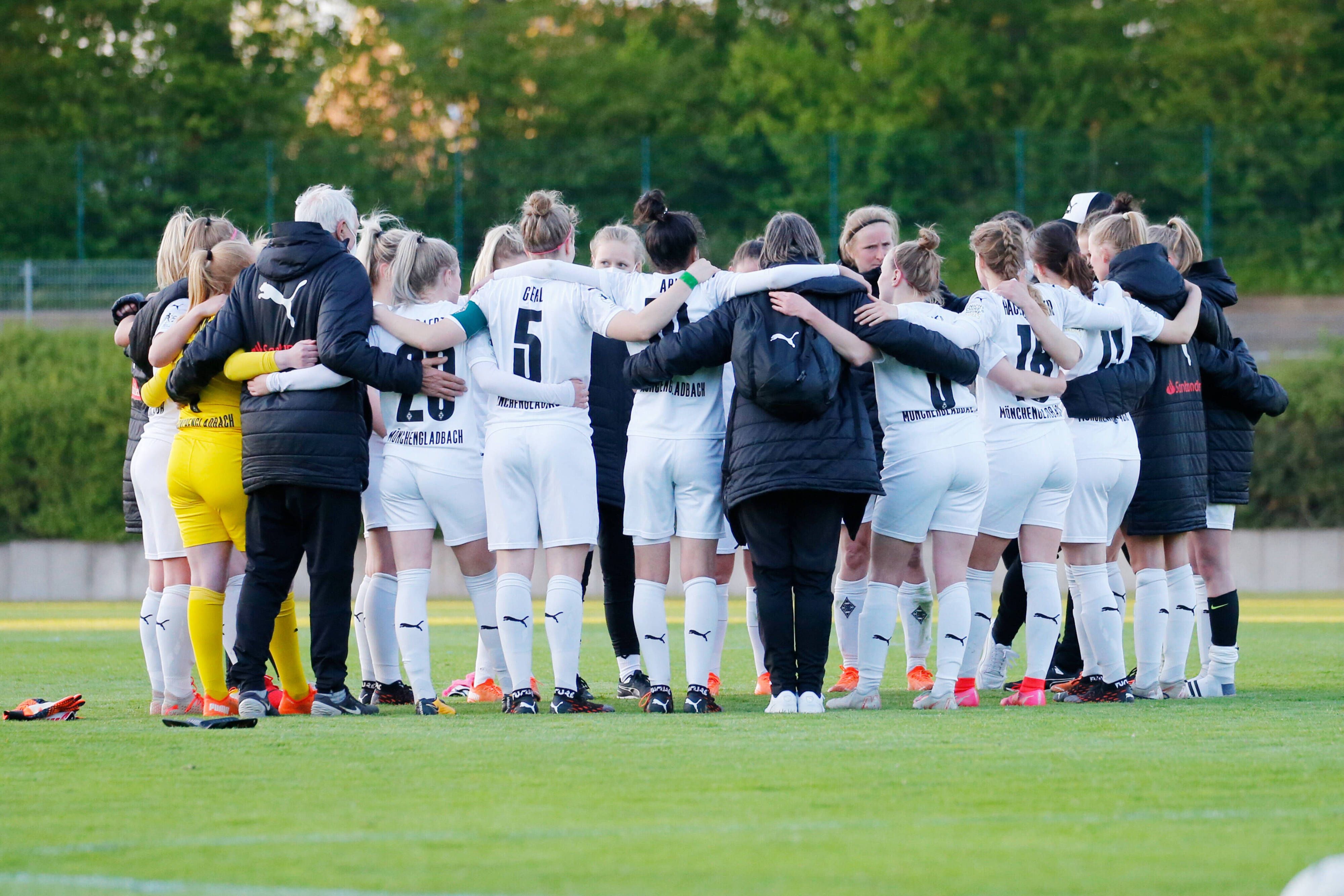 Das Team steht versammelt im Kreis, die Spielerinnen umarmen sich, einige sind nur von hinten zu sehen.