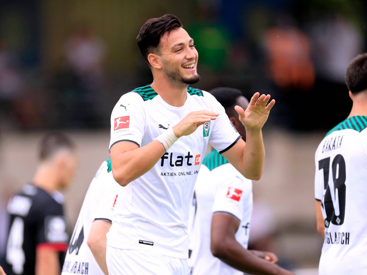 Ramy Bensebaini läuft lachend über den Fußballplatz und hält die Hände zum Abschlagen bereit.