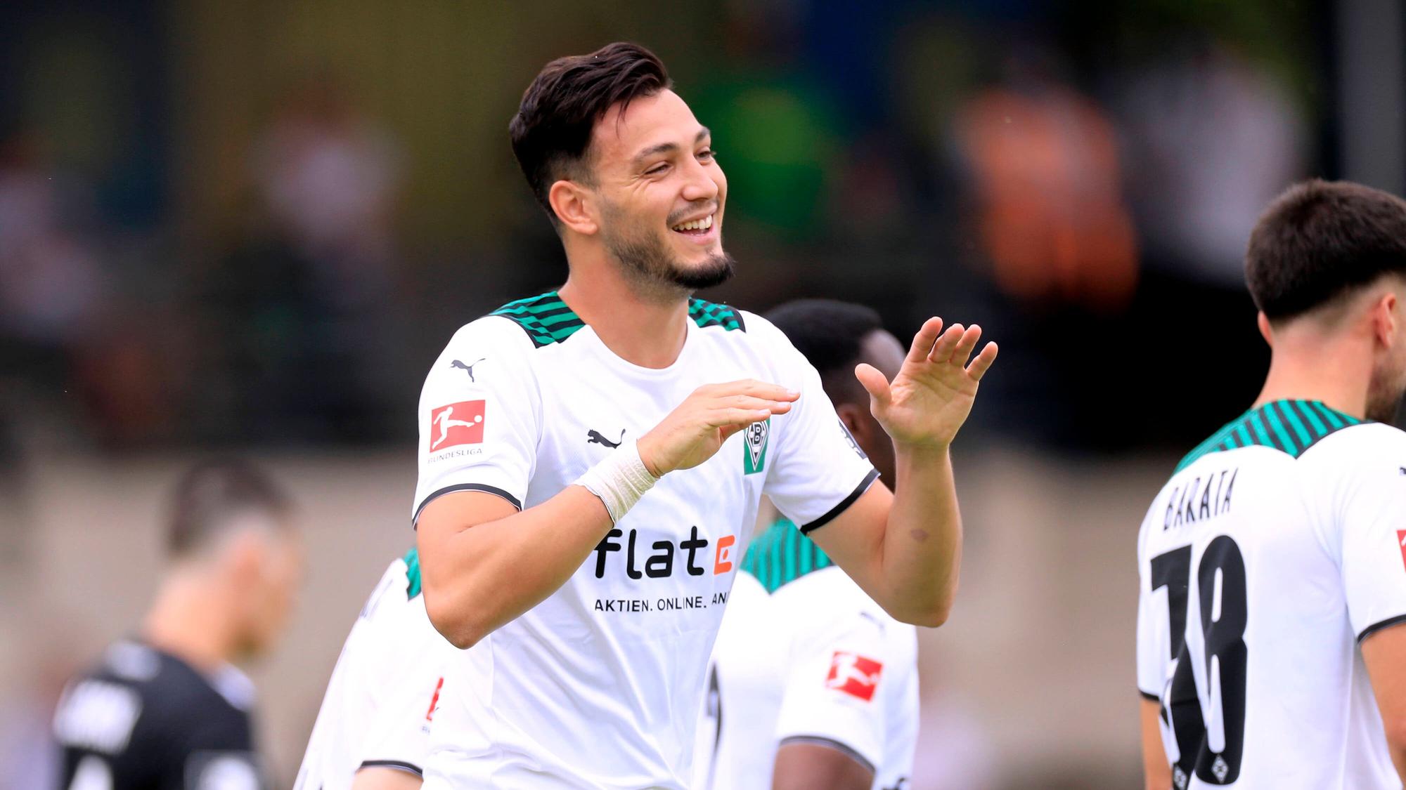 Ramy Bensebaini läuft lachend über den Fußballplatz und hält die Hände zum Abschlagen bereit.