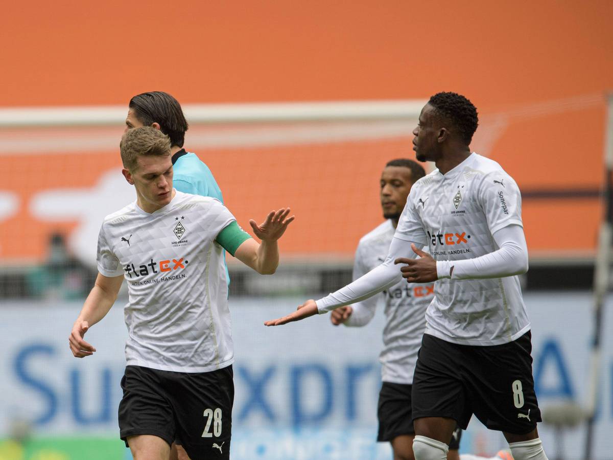 Matthias Ginter (l.) und Denis Zakaria laufen nebeneinander her, während Ginter in Zakarias Hand einschlägt.