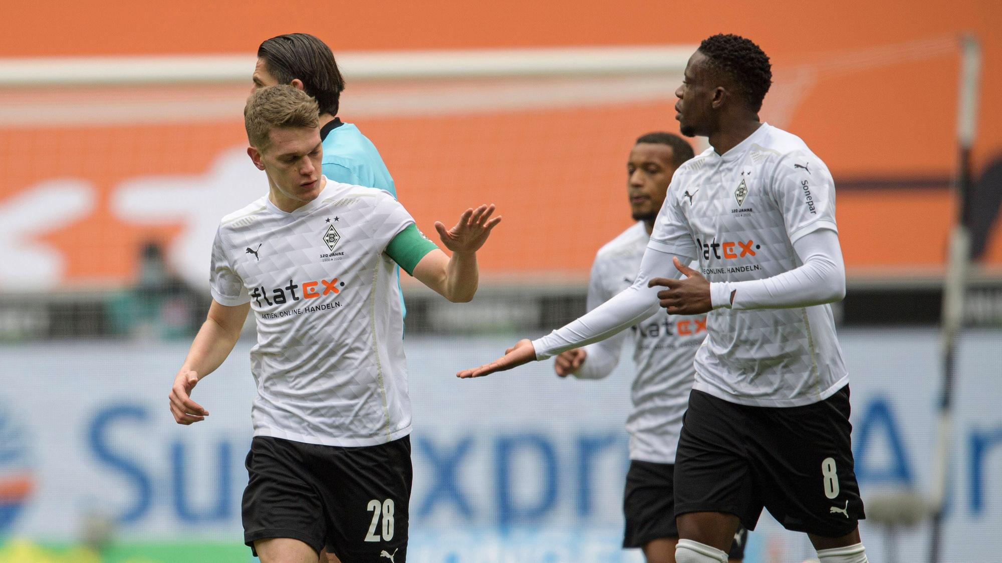 Matthias Ginter (l.) und Denis Zakaria laufen nebeneinander her, während Ginter in Zakarias Hand einschlägt.