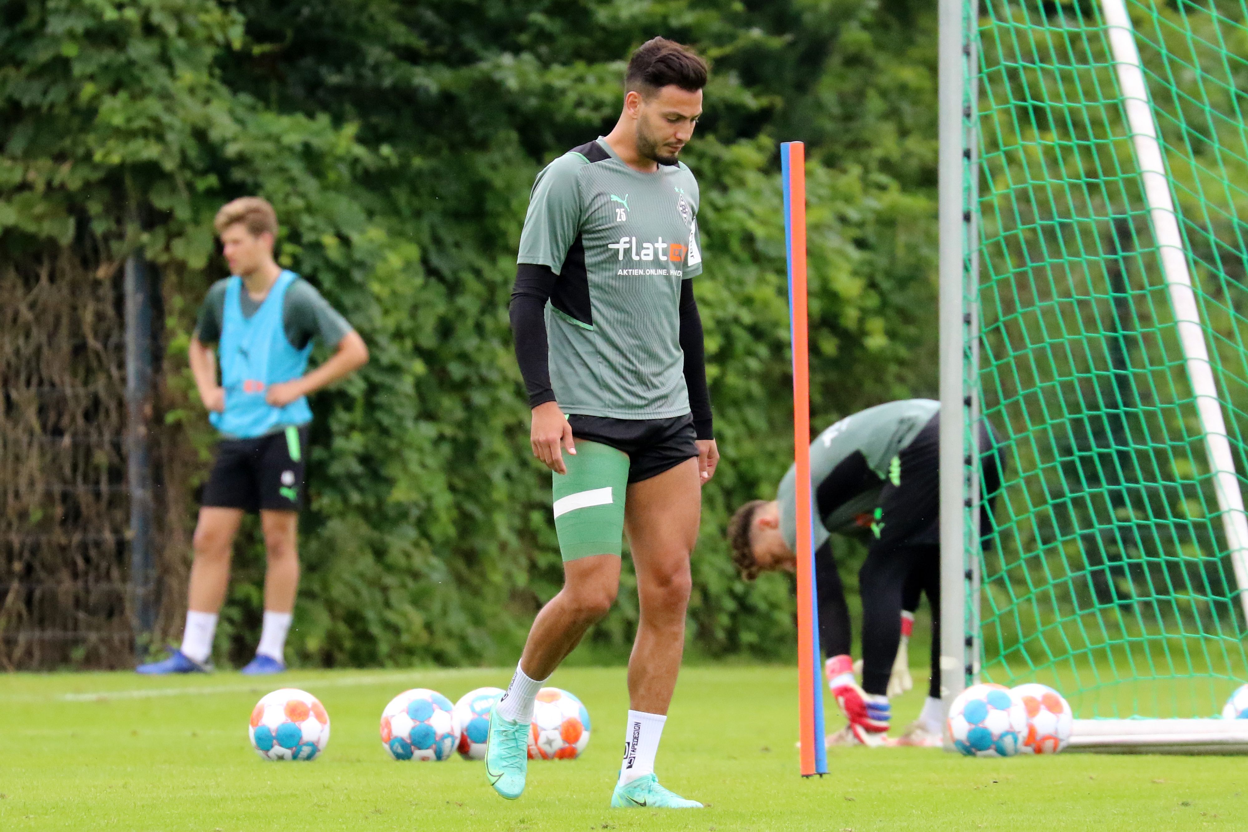 Ramy Bensebaini läuft mit hängendem Kopf und grüner Bandage um den verletzten Oberschenkel vom Trainingsplatz.