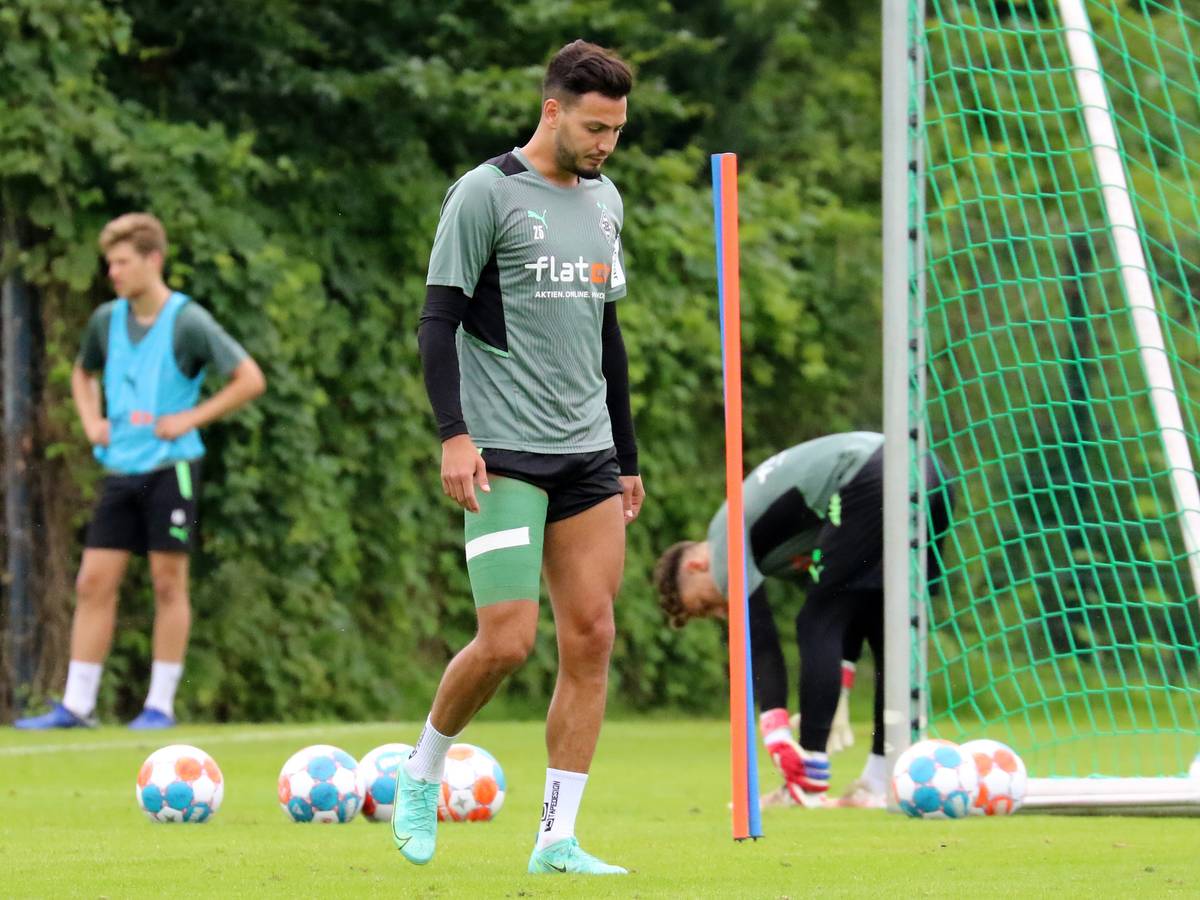 Ramy Bensebaini läuft mit hängendem Kopf und grüner Bandage um den verletzten Oberschenkel vom Trainingsplatz.