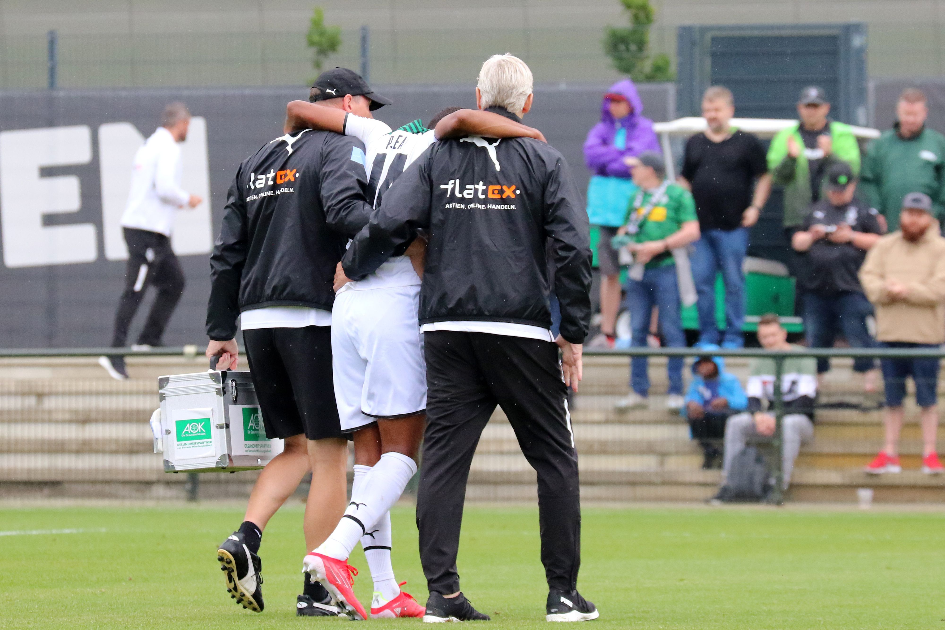 Gladbach-Stürmer Alassane Plea verletzte sich am Samstag (25. Juli 2021) beim Testspiel gegen den FC Metz am Knie und musste das Feld verlassen. Das Foto zeigt ihn humpelnd und gestützt von zwei Borussia-Verantwortlichen.