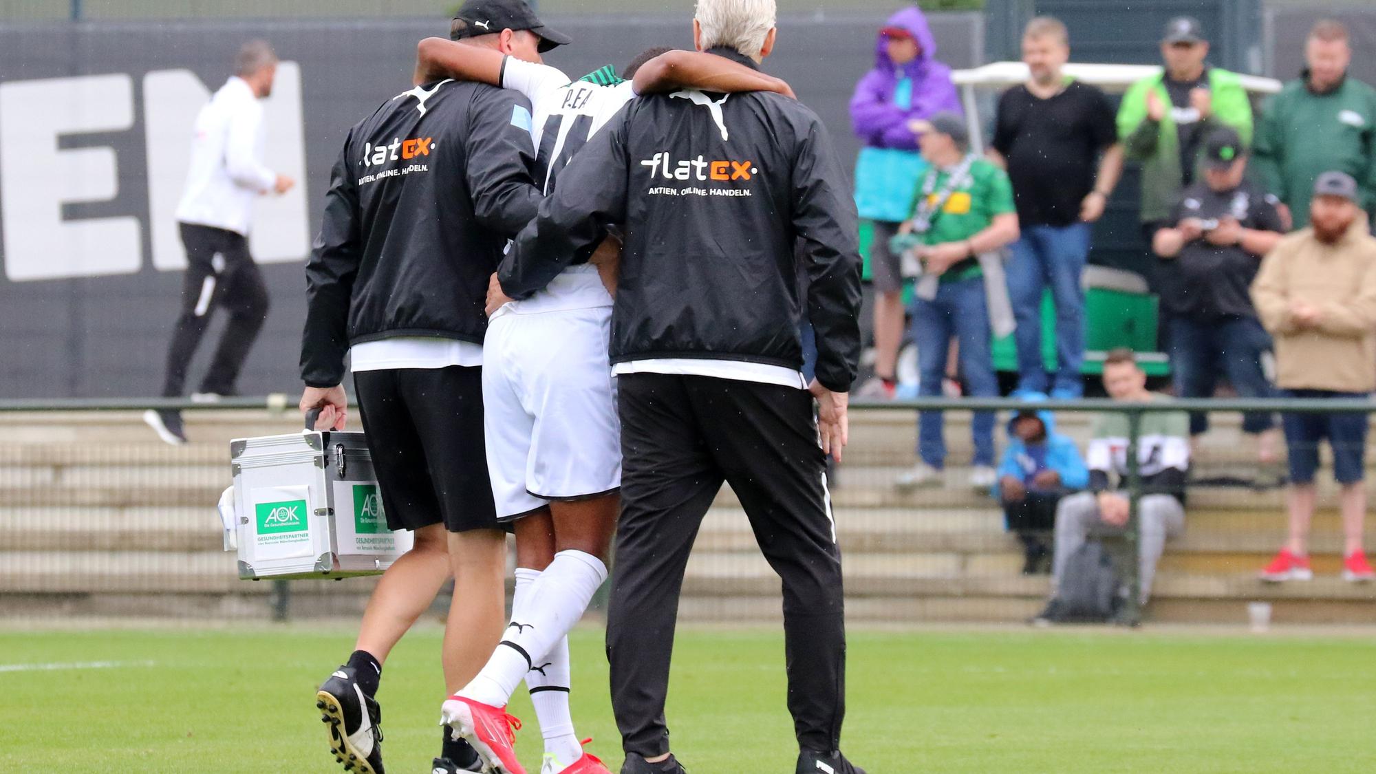 Gladbach-Stürmer Alassane Plea verletzte sich am Samstag (25. Juli 2021) beim Testspiel gegen den FC Metz am Knie und musste das Feld verlassen. Das Foto zeigt ihn humpelnd und gestützt von zwei Borussia-Verantwortlichen.