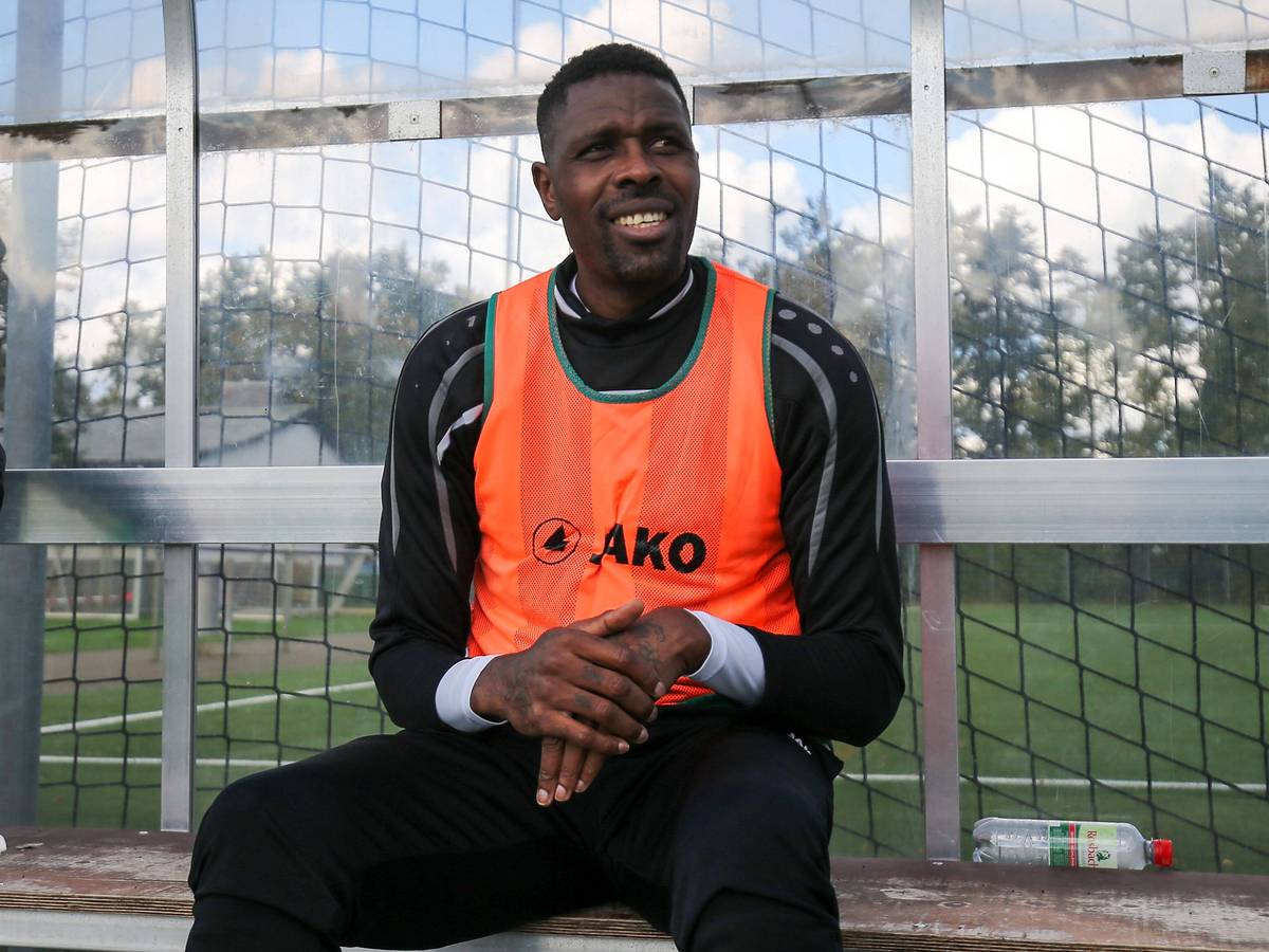Ex-Gladbacher Mo Idrissou sitz am 10. Oktober 2020 im orangenen Leibchen beim Spiel gegen den Hunfelder SV auf der Ersatzbank beim SC Viktoria Griesheim und lächelt.