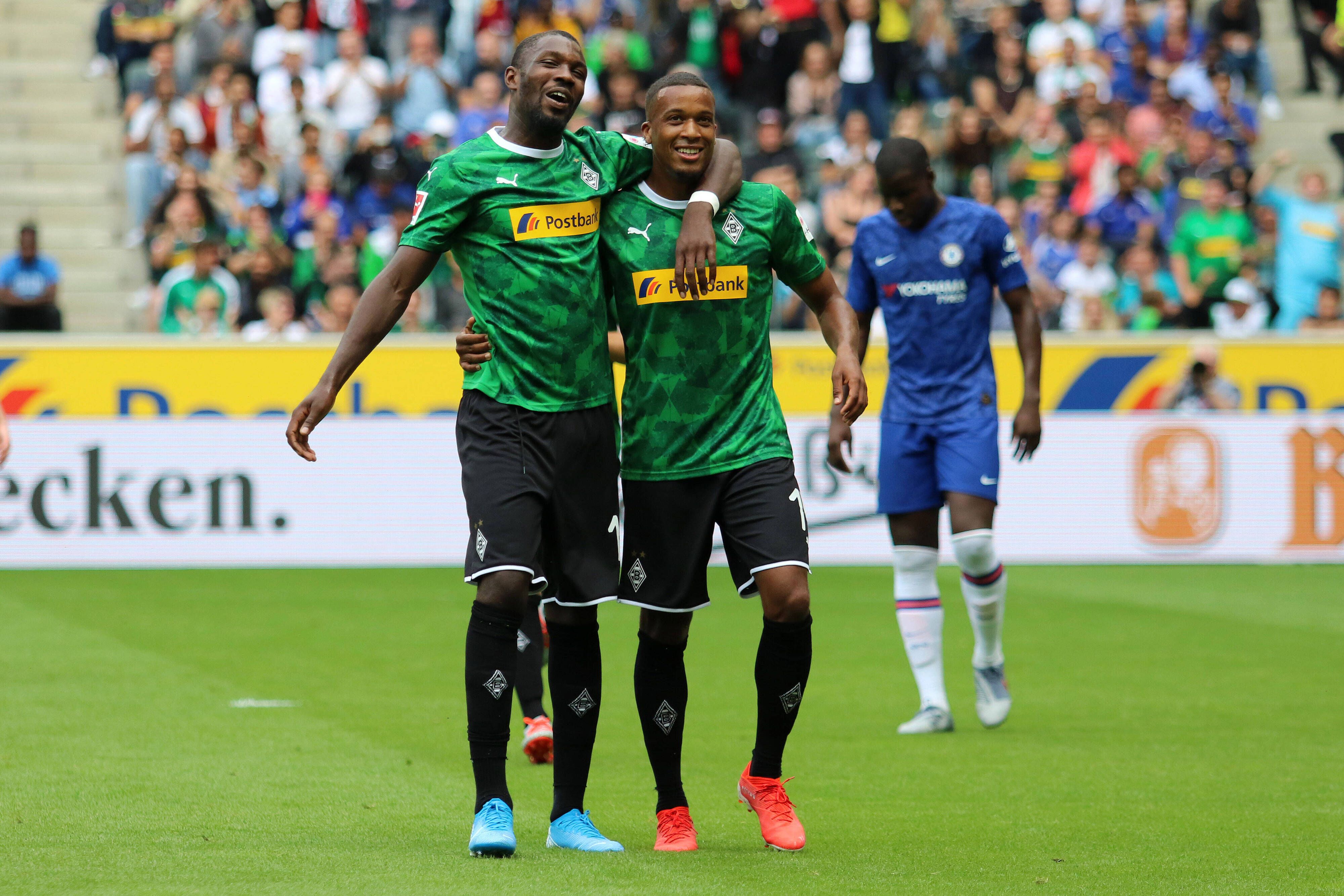 Thuram und Plea laufen Arm in Arm über den grünen Rasen des Fußballplatzes, sie tragen das grüne Gladbach-Trikot.