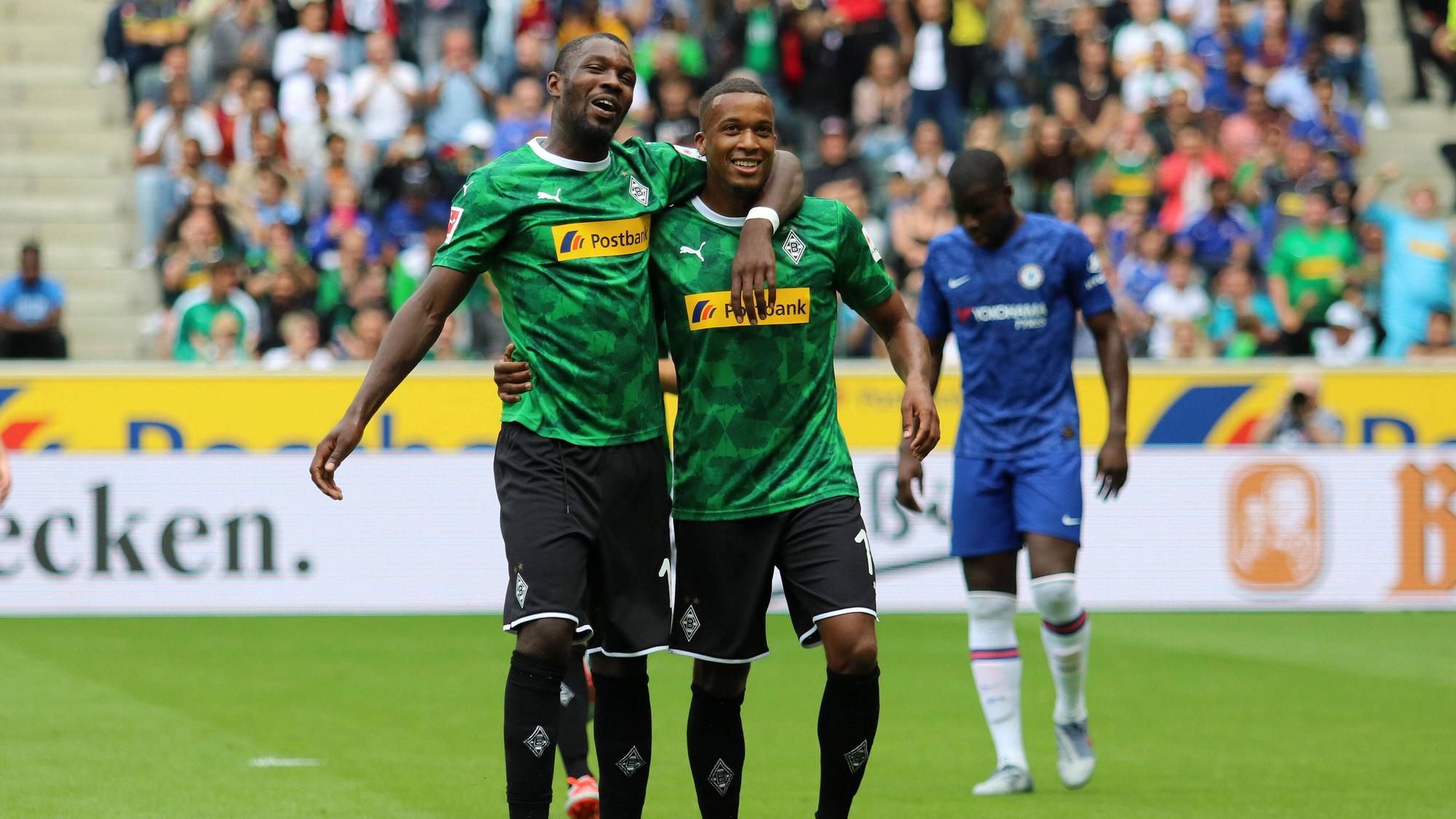 Thuram und Plea laufen Arm in Arm über den grünen Rasen des Fußballplatzes, sie tragen das grüne Gladbach-Trikot.