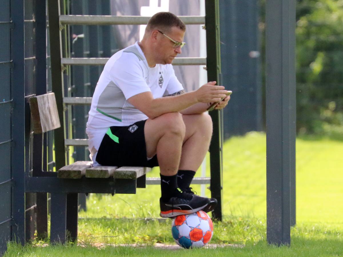 Gladbach-Manager Max Eberl sitzt auf einer Bank, derweil schaut er auf sein Smartphone. Seine Füße ruhen auf einem Fußball.