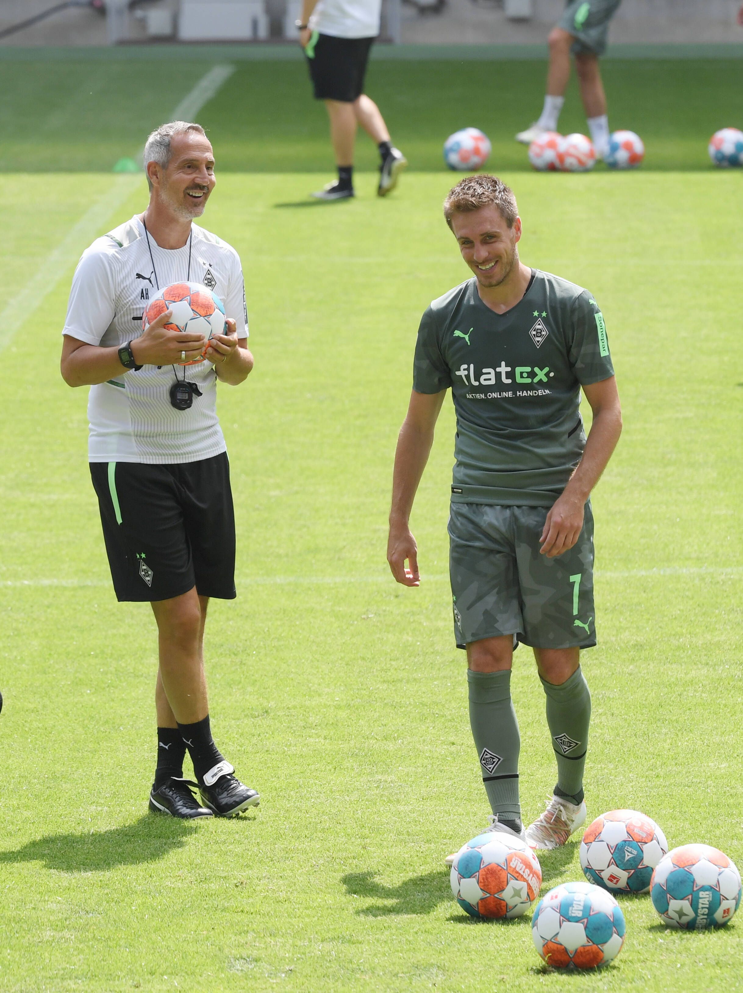 Adi Hütter (l.) mit einem Ball in der Hand und Patrick Herrmann (r.) lachen.