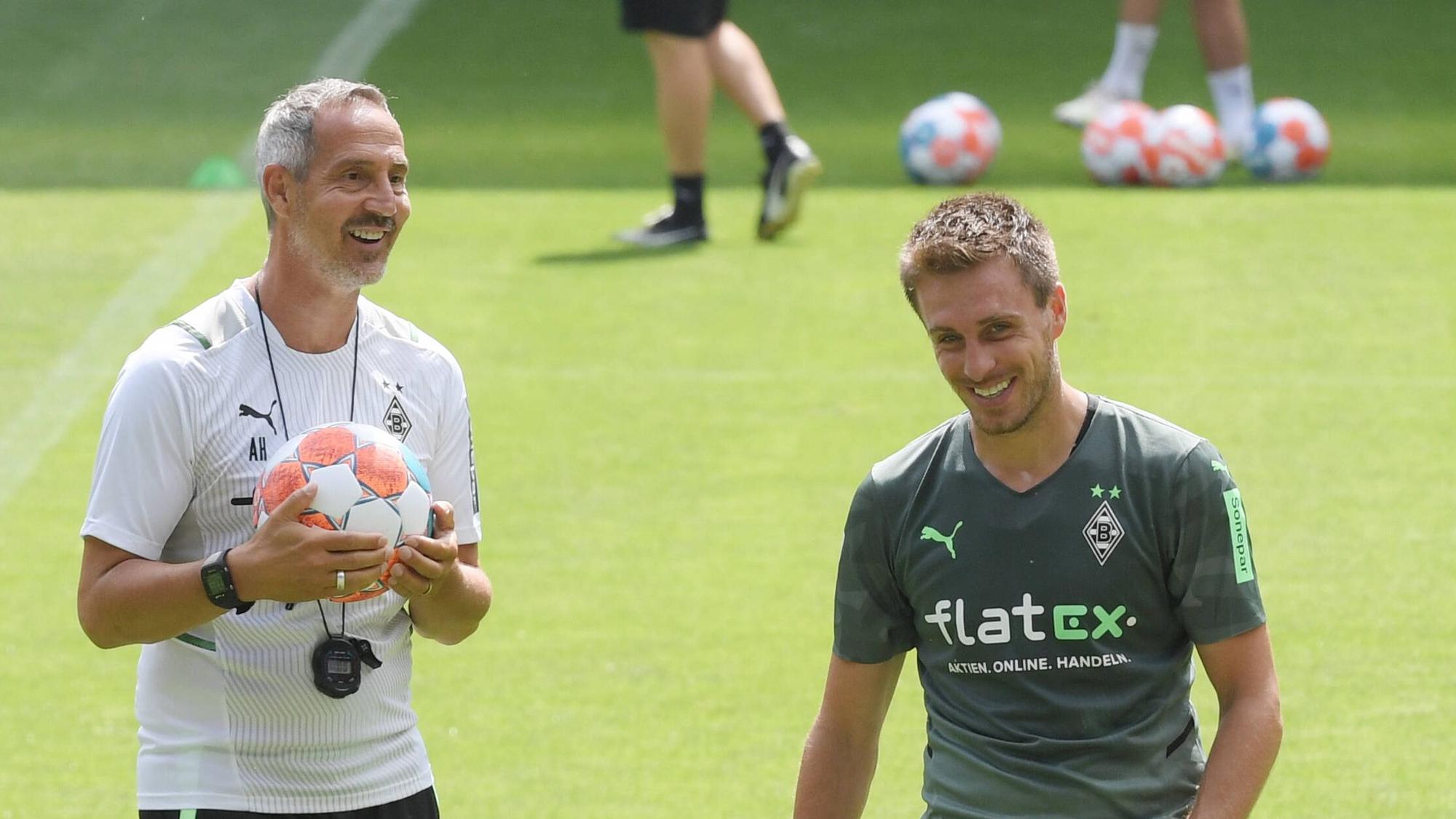 Adi Hütter (l.) mit einem Ball in der Hand und Patrick Herrmann (r.) lachen.