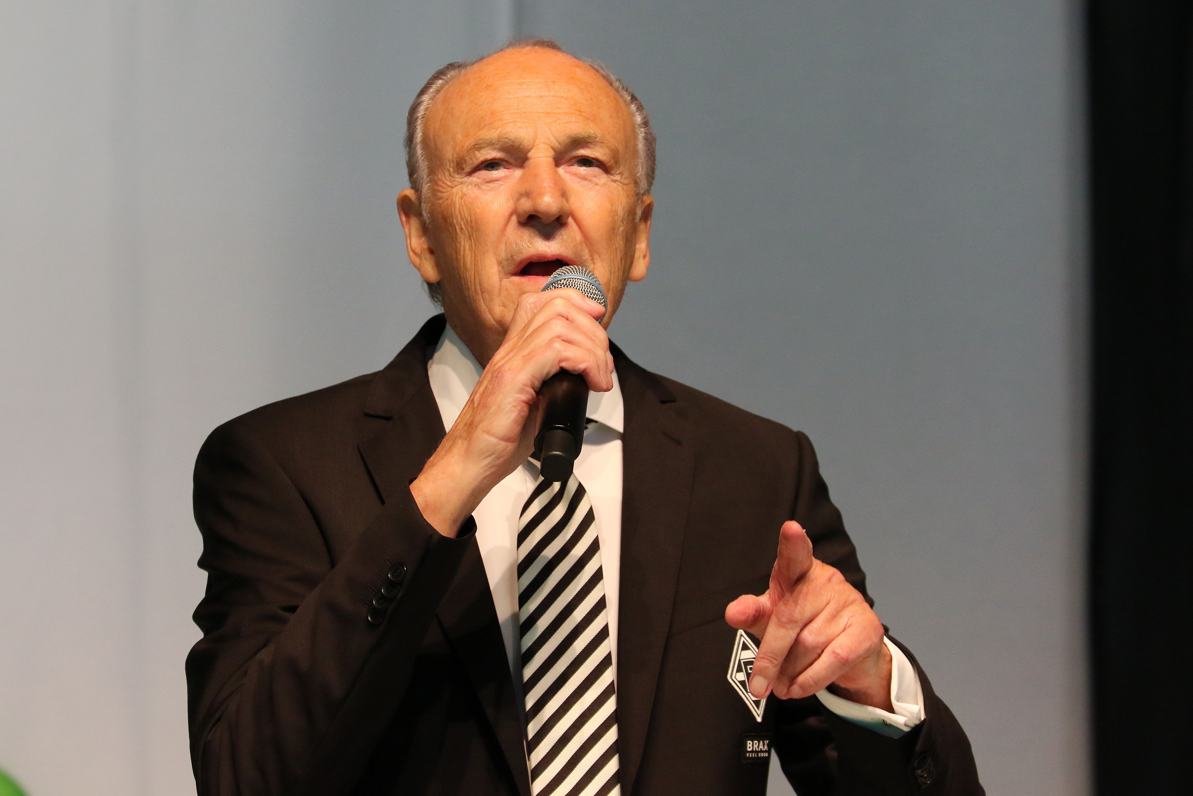 Borussias Präsident Rolf Königs bei der Mitgliederversammlung am 10. August 2021 im Gladbacher Stadion. Der 79-Jährige hält in der rechten Hand ein Mikro, mit der linken Hand deutet er in Richtung Zuhörer.