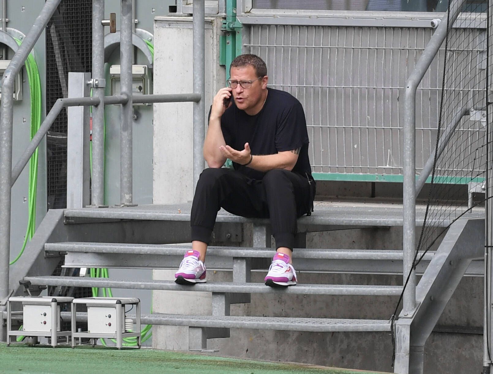Gladbach-Manager Max Eberl sitzt auf einer Metalltreppe im Borussia-Park, derweil telefoniert er mit seinem Smartphone, mit der linken Hand gestikuliert er.