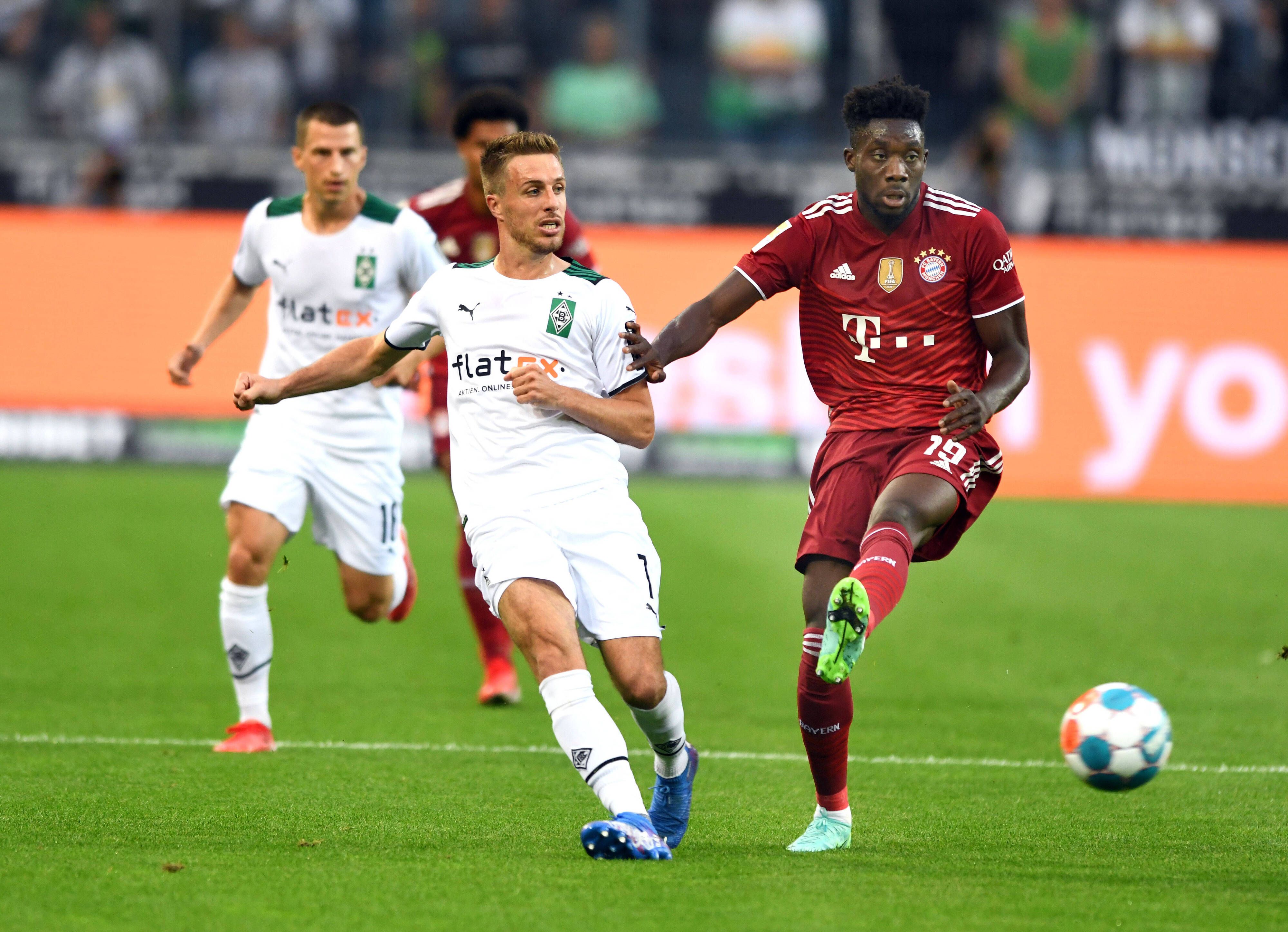 Gladbachs Patrick Herrmann (l.) am 13. August 2021 im Zweikampf mit Bayerns Alphonso Davies (r.) beim Bundesliga-Auftakt-Match im Borussia-Park.