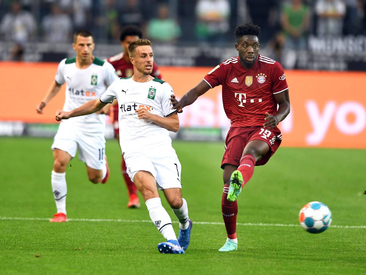 Gladbachs Patrick Herrmann (l.) am 13. August 2021 im Zweikampf mit Bayerns Alphonso Davies (r.) beim Bundesliga-Auftakt-Match im Borussia-Park.