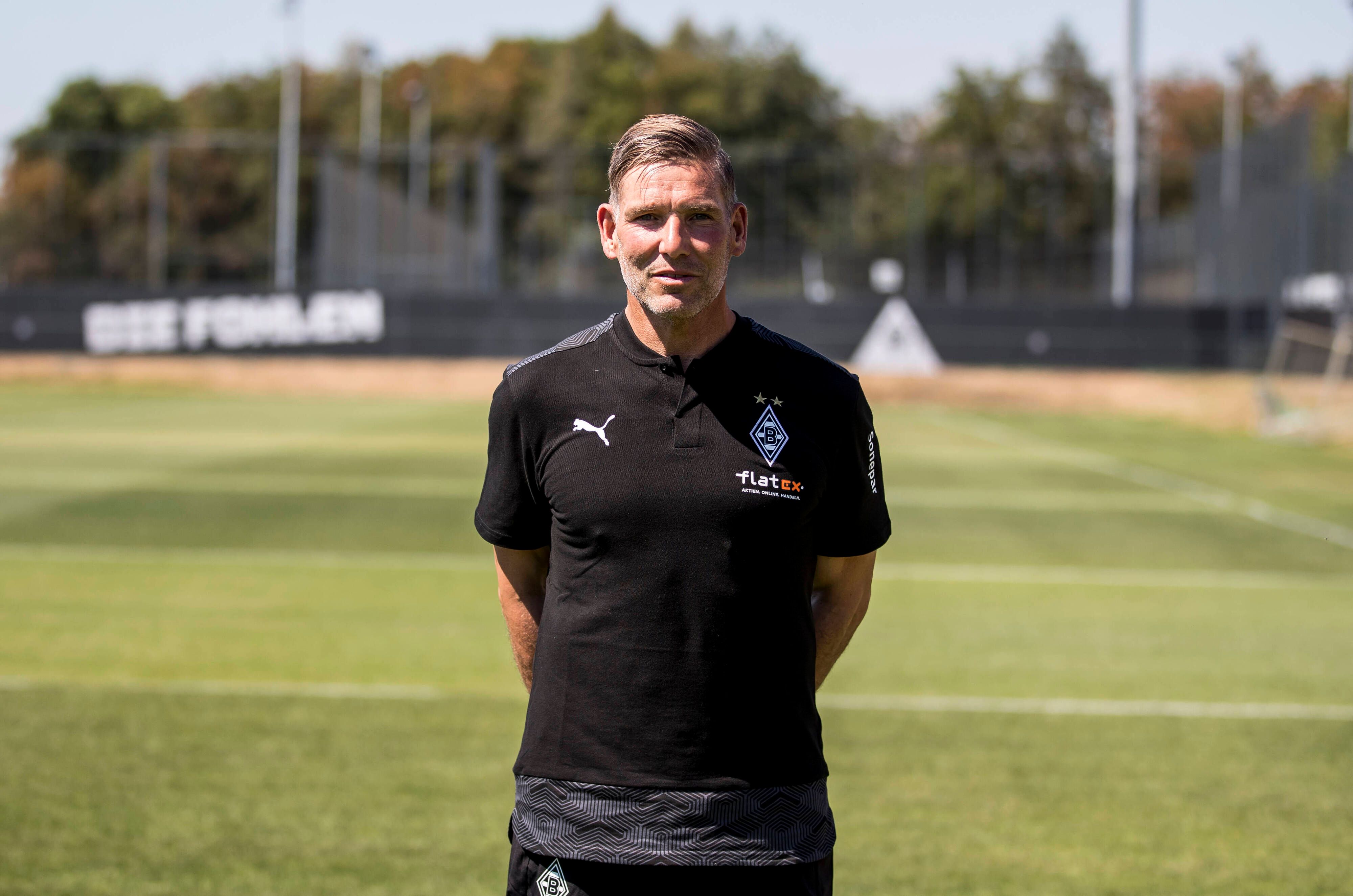 Gladbach-Legende und Torwarttrainer Uwe Kamps blickt in die Kamera, seine Arme hat er auf dem Rücken verschränkt.