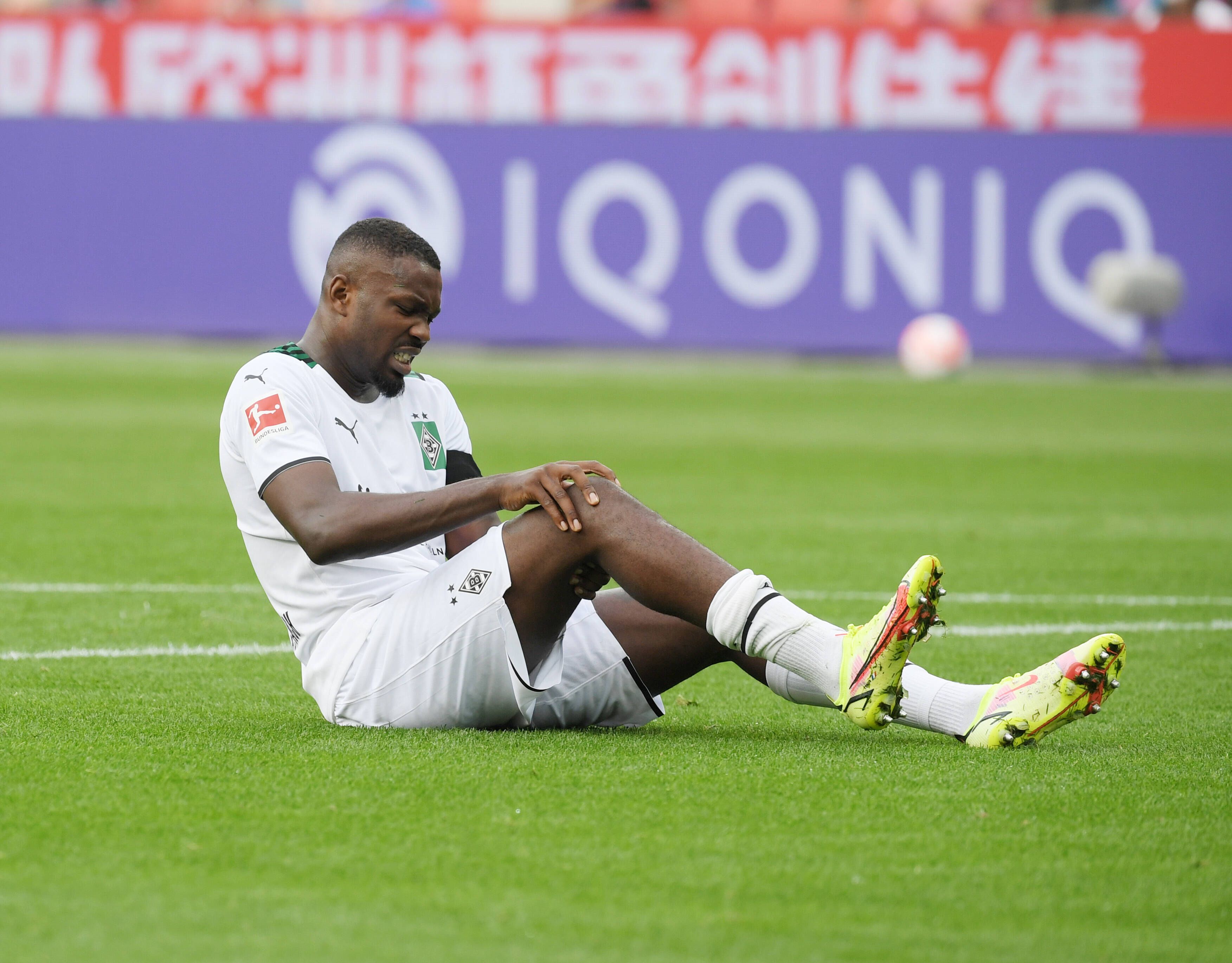 Gladbachs Marcus Thuram sitzt beim Bundesliga-Spiel in Leverkusen am 21. August 2021 verletzt auf dem Feld und hält sich das Knie.