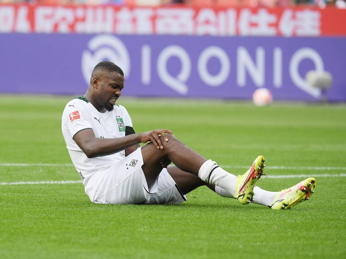 Gladbachs Marcus Thuram sitzt beim Bundesliga-Spiel in Leverkusen am 21. August 2021 verletzt auf dem Feld und hält sich das Knie.