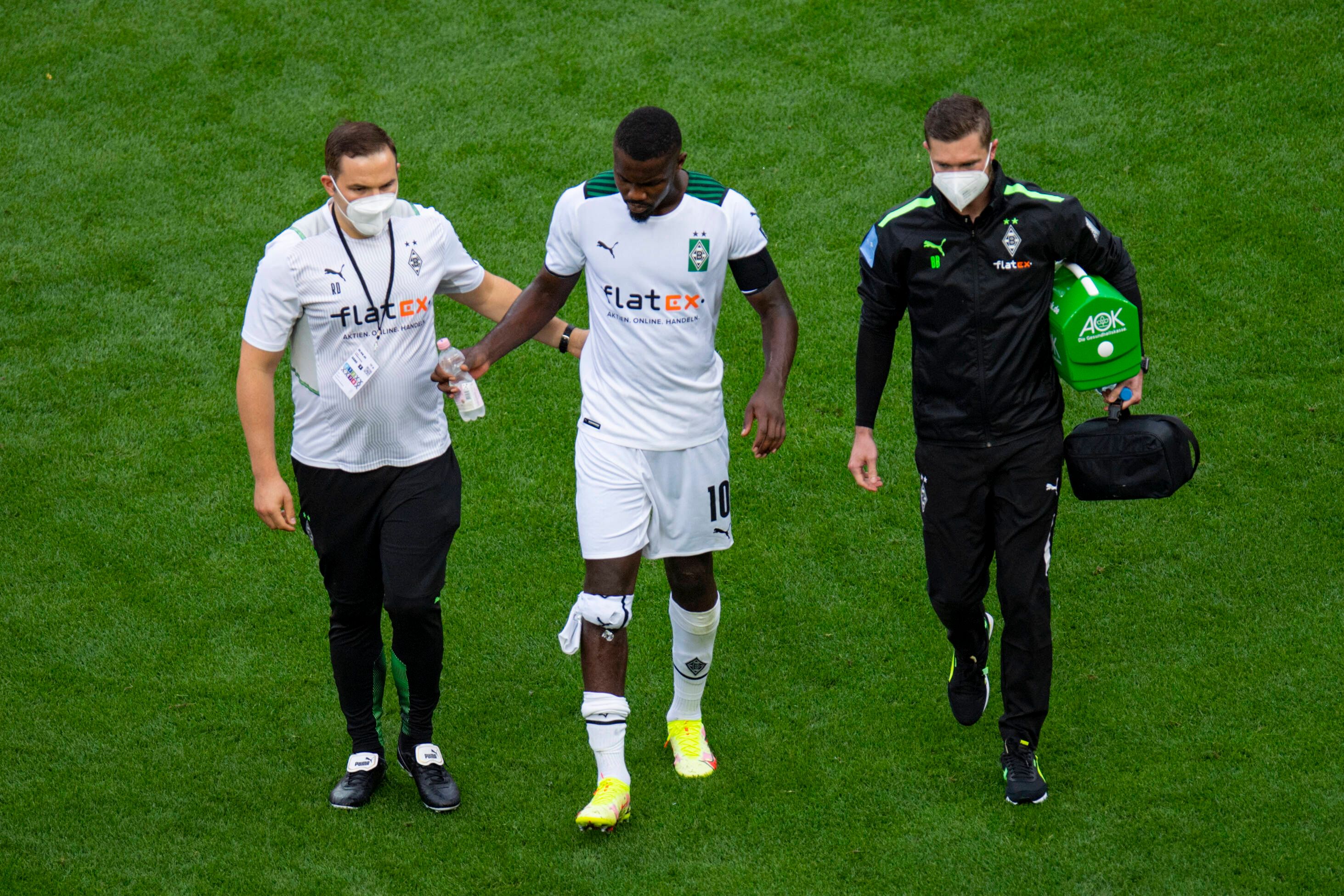 Gladbach-Stürmer Marcus Thuram (Mitte) humpelt beim verlorenen Rheinland-Duell (0:4) der Borussia in Leverkusen (21. August 2021) frühzeitig verletzt vom Platz. Er wird von zwei Betreuern, die eine Maske tragen, begleitet.