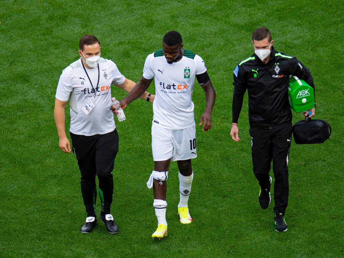 Gladbach-Stürmer Marcus Thuram (Mitte) humpelt beim verlorenen Rheinland-Duell (0:4) der Borussia in Leverkusen (21. August 2021) frühzeitig verletzt vom Platz. Er wird von zwei Betreuern, die eine Maske tragen, begleitet.