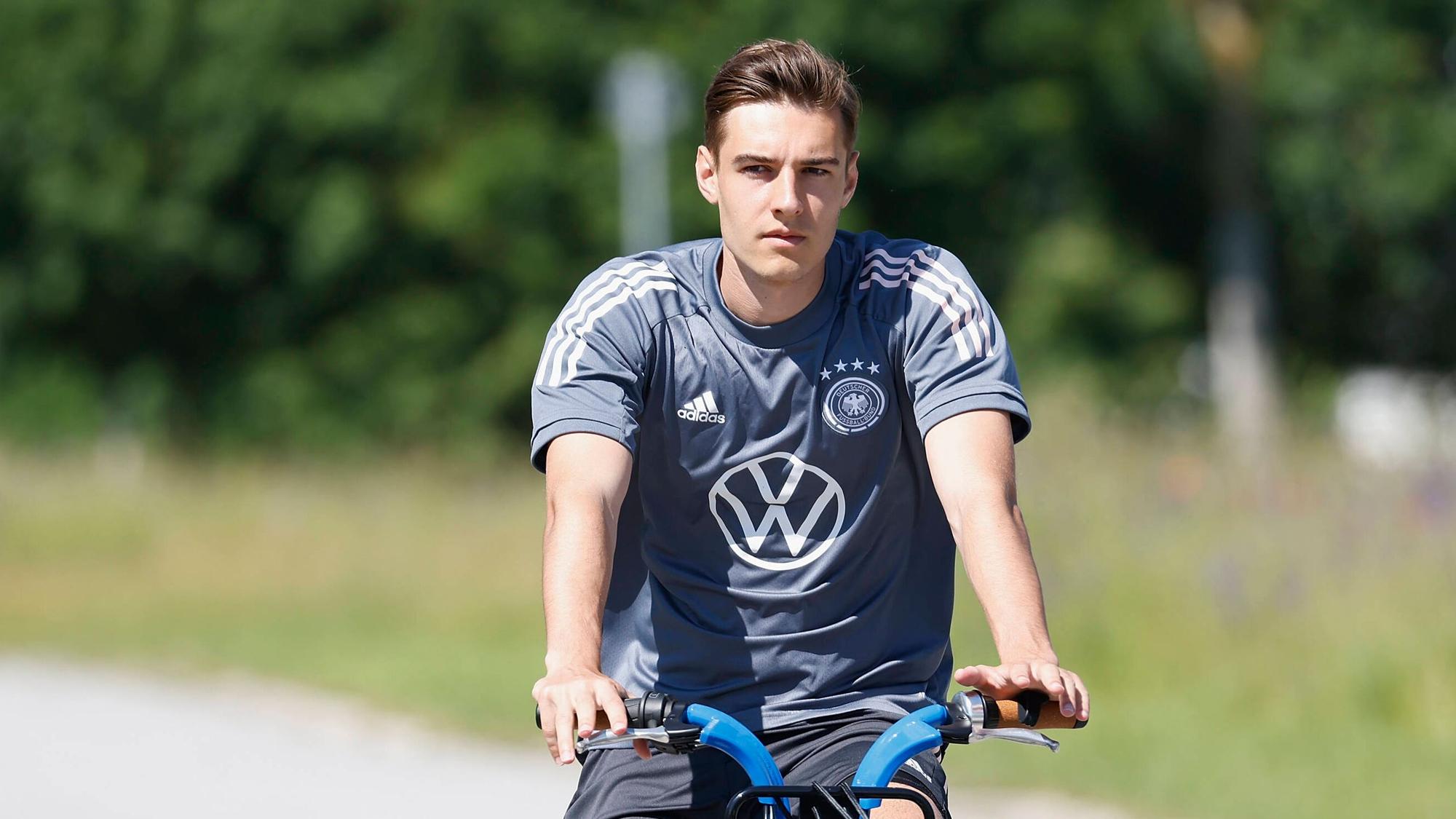 Gladbachs Nationalspieler Florian Neuhaus, hier zu sehen bei einer Radtour während des DFB-Trainingslagers in Herzogenaurach am 17. Juni 2021. Neuhaus sitzt auf einem Rand und schaut in die Kamera.