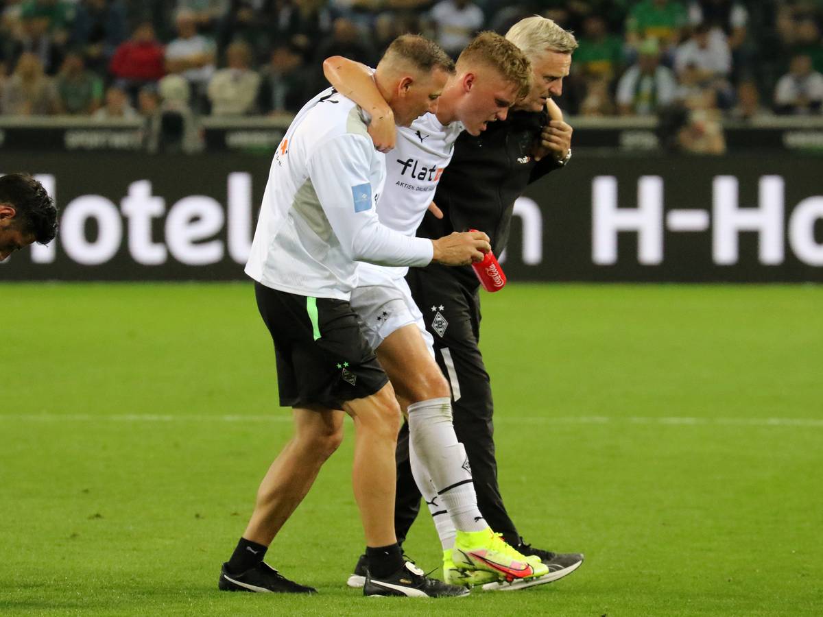 Luca Netz (M.), Spieler von Borussia Mönchengladbach, muss beim Bundesliga-Duell gegen Arminia Bielefeld (12. September 2021) verletzt vom Platz. Physio Dirk Müller (l.) und Team-Arzt Stefan Hertl (r.) stützen den Außenbahnspieler.