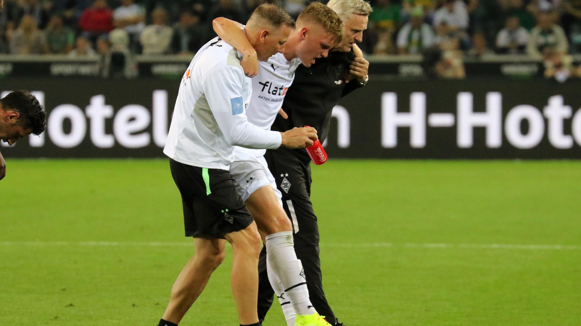 Luca Netz (M.), Spieler von Borussia Mönchengladbach, muss beim Bundesliga-Duell gegen Arminia Bielefeld (12. September 2021) verletzt vom Platz. Physio Dirk Müller (l.) und Team-Arzt Stefan Hertl (r.) stützen den Außenbahnspieler.