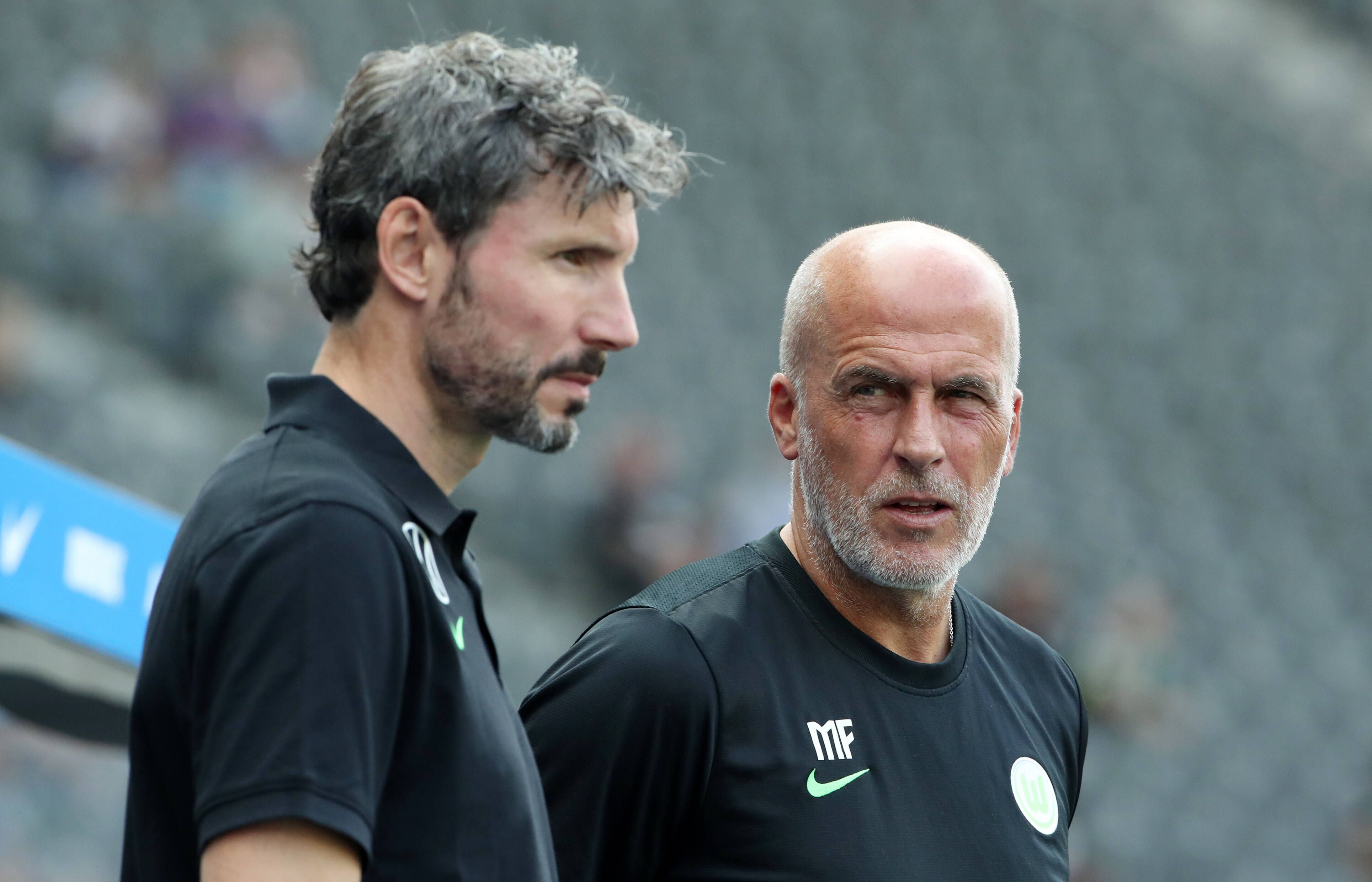 Ex-Gladbach-Trainer Michael Frontzeck (r.) arbeitet aktuell als Co-Trainer unter Mark van Bommel (l.) beim Fußball-Bundesligisten VfL Wolfsburg. Auf diesem Foto sind die beiden am 21. August 2021 im Berliner Olympiastadion zu sehen. Frontzeck blickt zu van Bommel rüber.