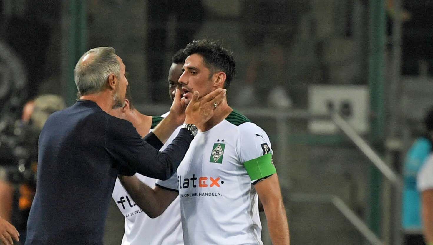 Gladbach-Coach Adi Hütter (l.), jüngst von den Profifußballern in Deutschland zum Trainer der vergangenen Saison gewählt worden, spricht am 12. September 2021 mit seinem Kapitän Lars Stindl, der Borussias Jahrtausend-Torschütze ist. Hütter fasst Stindl mit den Händen ins Gesicht.