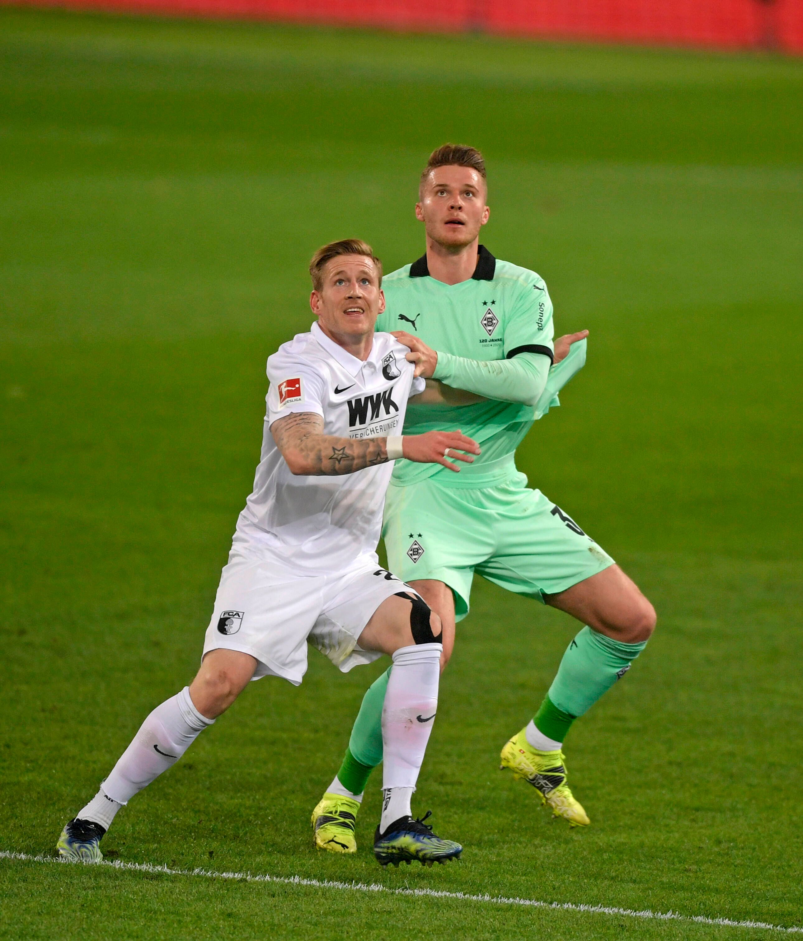 Nico Elvedi (r.), Spieler von Borussia Mönchengladbach und Andre Hahn (l.) blicken im Zweikampf um den Ball nach oben, im Aufeinandertreffen beider Klubs am 12. März 2021.