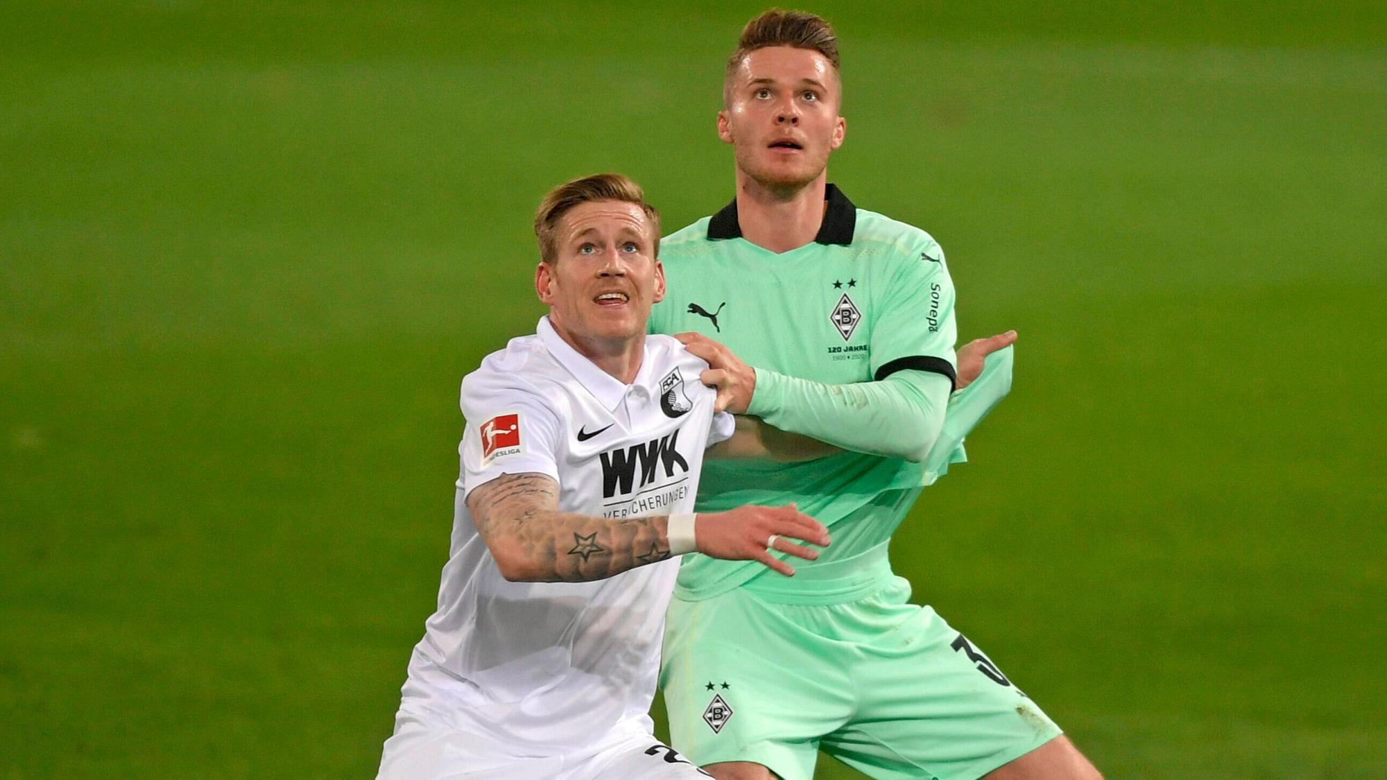 Nico Elvedi (r.), Spieler von Borussia Mönchengladbach und Andre Hahn (l.) blicken im Zweikampf um den Ball nach oben, im Aufeinandertreffen beider Klubs am 12. März 2021.