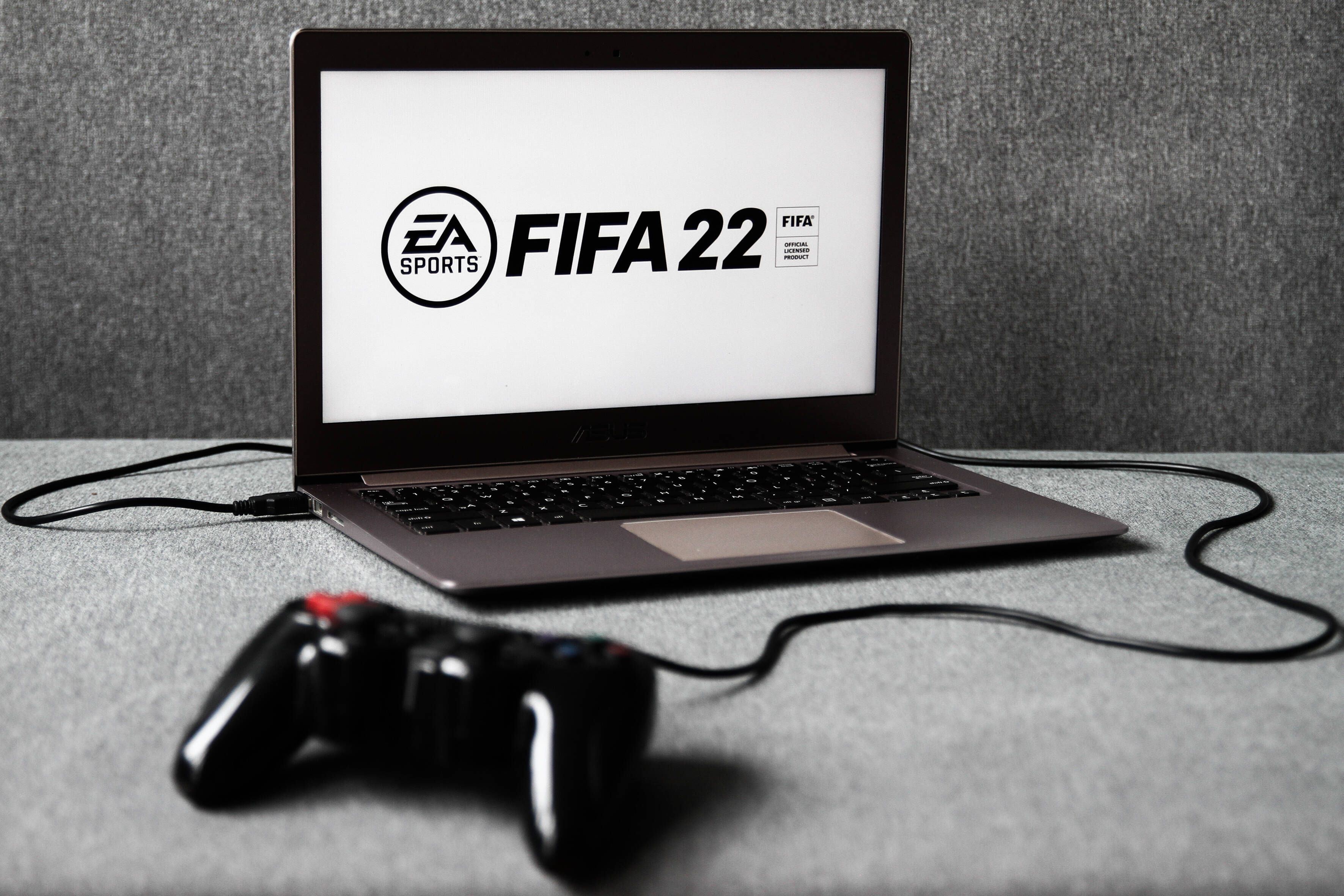 Das Logo des am 1. Oktober 2021 erscheinenden Fußball-Konsolen-Spiels FIFA 22  ist auf einem Laptop zu sehen, an den ein Controller angeschlossen ist.