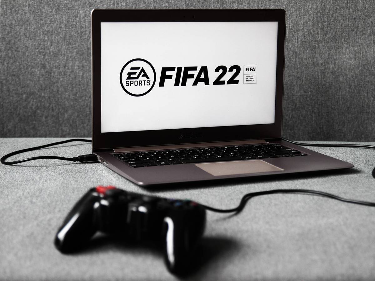 Das Logo des am 1. Oktober 2021 erscheinenden Fußball-Konsolen-Spiels FIFA 22 ist auf einem Laptop zu sehen, an den ein Controller angeschlossen ist.