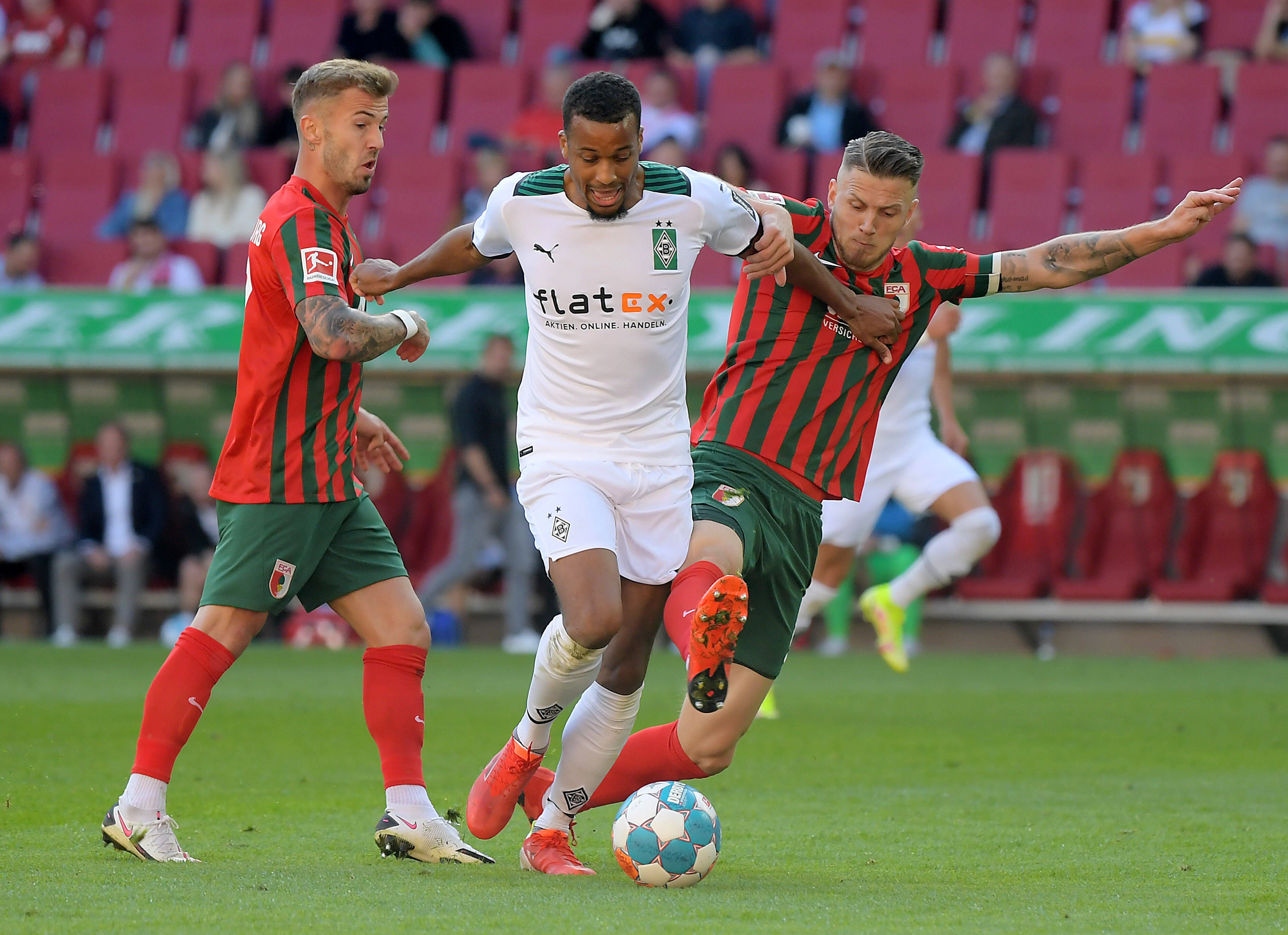 Alassane Plea von Borussia Mönchengladbach versucht seine beiden Augsburger Gegenspieler mit ausgestreckten Armen von sich wegzuhalten im Spiel gegen den FCA am 18. September 2021.