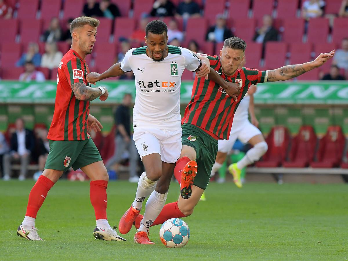 Alassane Plea von Borussia Mönchengladbach versucht seine beiden Augsburger Gegenspieler mit ausgestreckten Armen von sich wegzuhalten im Spiel gegen den FCA am 18. September 2021.
