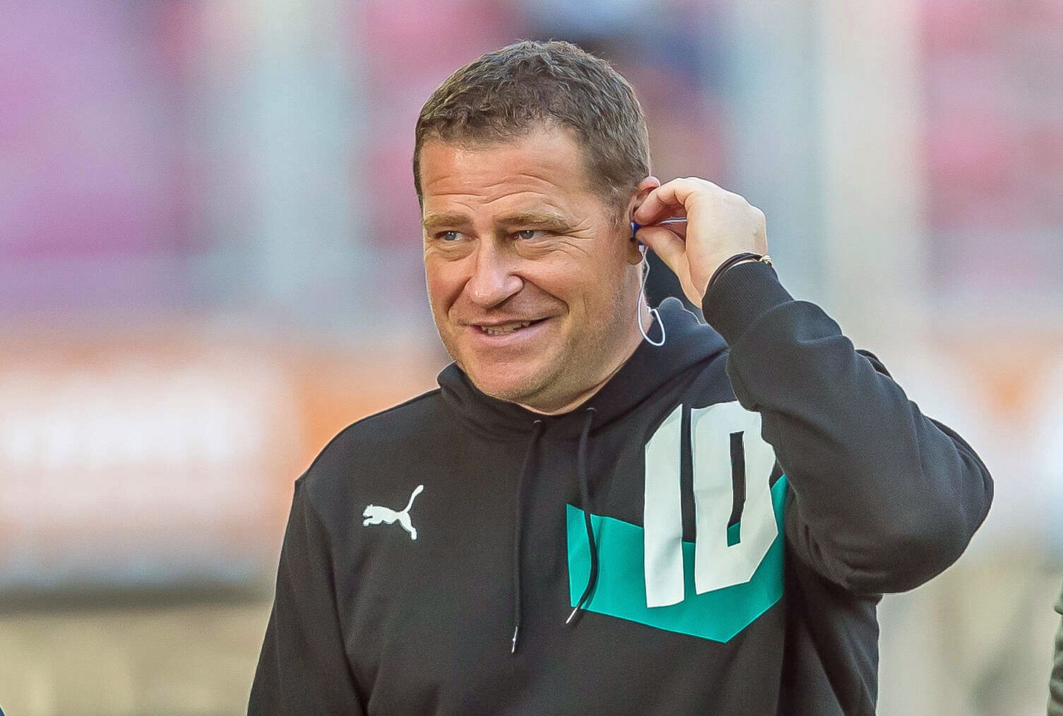 Gladbach-Manager Max Eberl. Auf diesem Foto ist der 47-Jährige am 18. September 2021 im Augsburger Stadion zu sehen. Eberl ist beim TV-Sender Sky zu Gast und bereitet sich auf ein Interview vor. In sein linkes Ohr steckt er einen Kopfhörer.