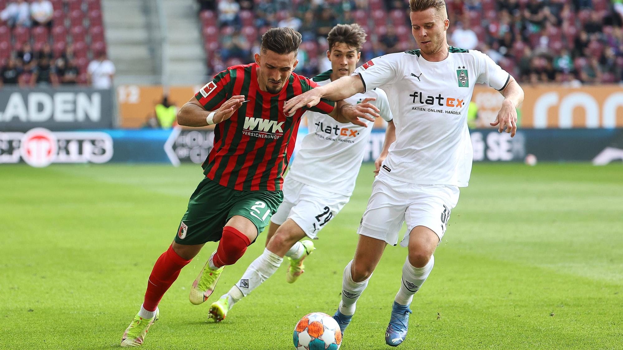 Nico Elvedi, Spieler von Borussia Mönchengladbach im Kampf um den Ball mit Andi Zeqiri vom FC Augsburg am 19. September 2021, dahinter kommt Joe Scally von Gladbach angelaufen.