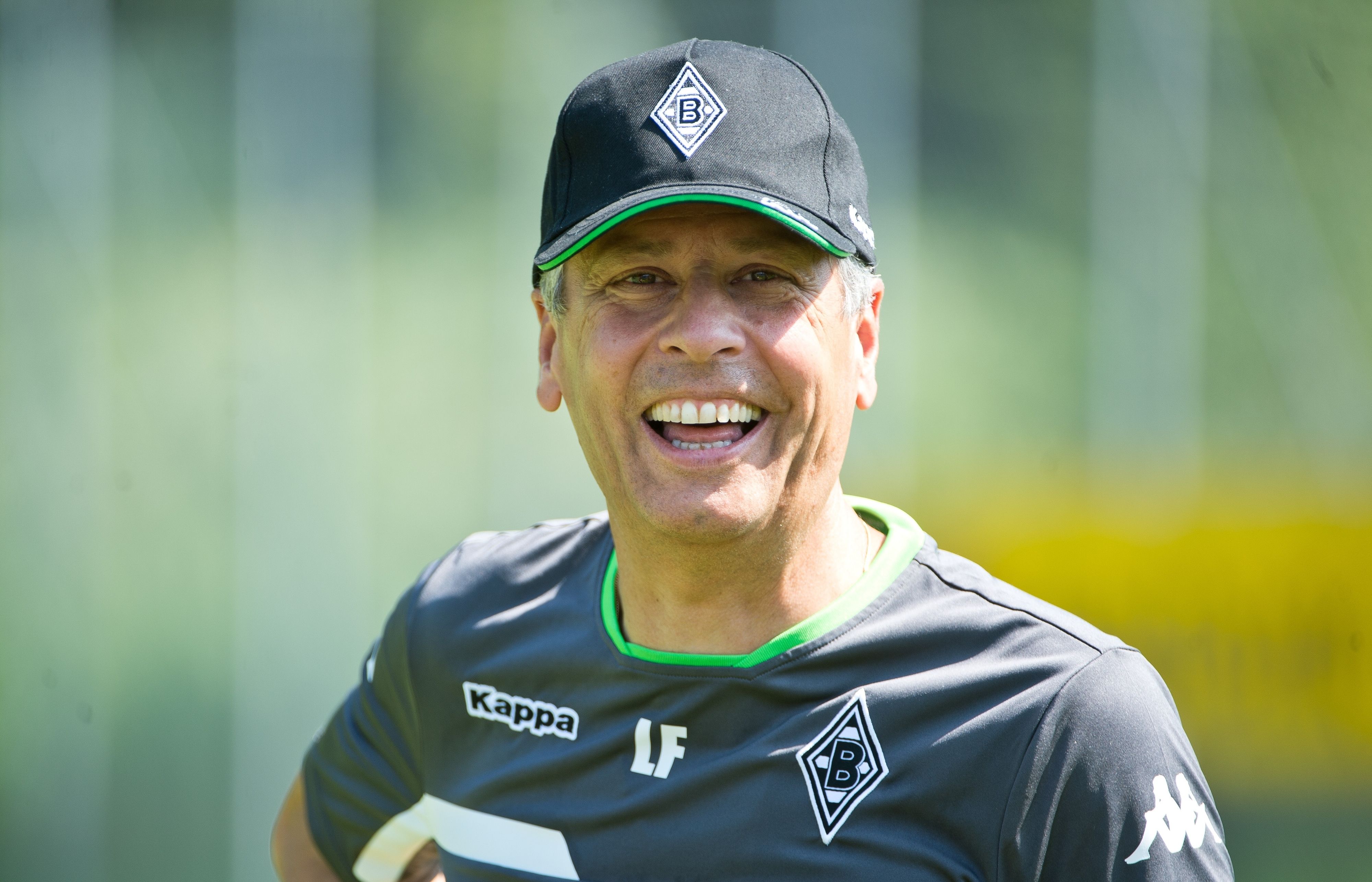 Lucien Favre lächelt als Trainer von Fußball-Bundesligist Borussia Mönchengladbach am 17. Juli 2015 während des Trainingslagers in Rottach-Egern (Bayern) in die Kamera. Er trägt dabei ein Kappe auf dem Kopf.
