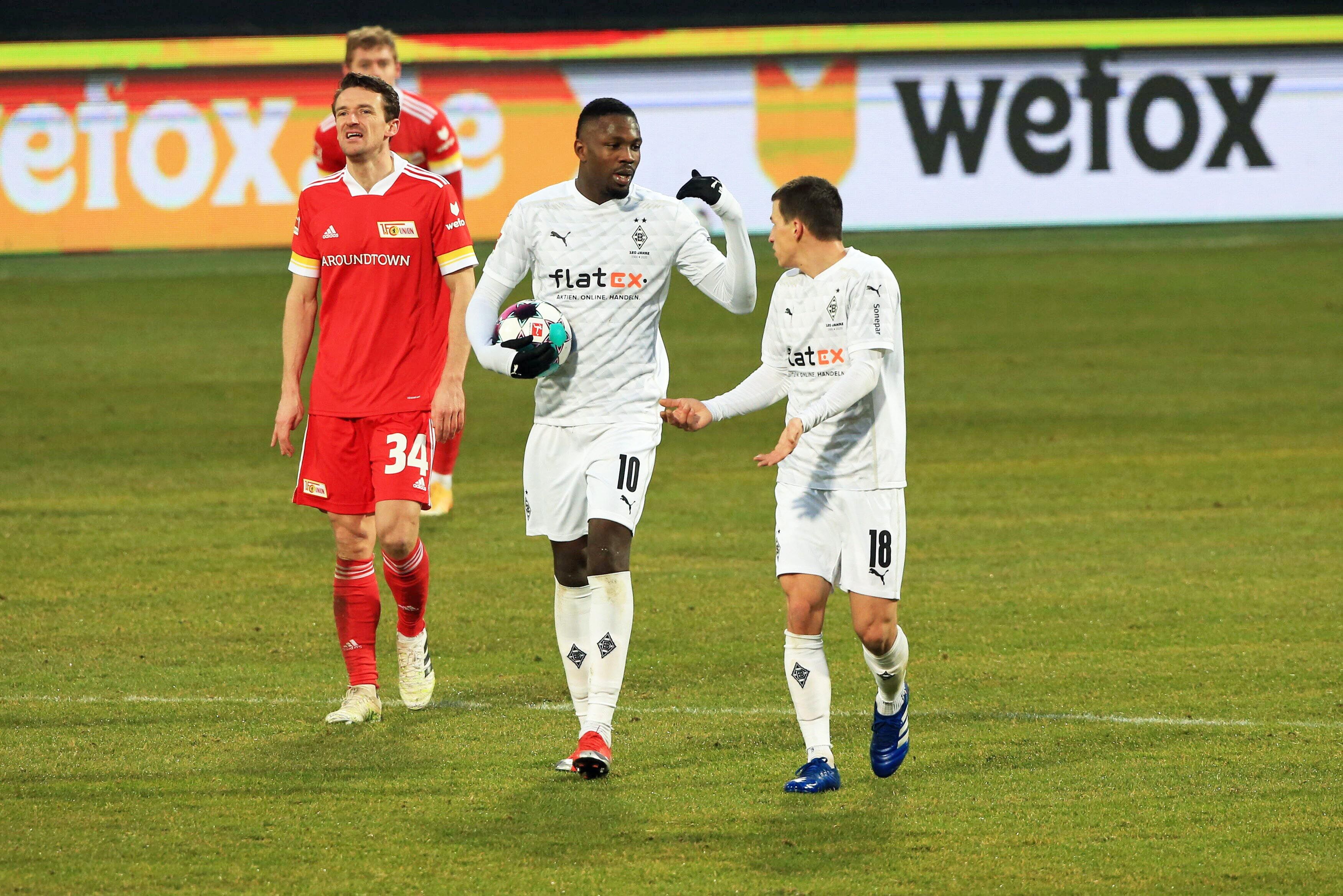Die Gladbacher Profis Marcus Thuram (M.) und Stefan Lainer (r.) unterhalten sich beim Bundesliga-Remis in Berlin am 30. Januar 2021 auf dem Spielfeld, Thuram trägt dabei den Ball in seinen Händen.