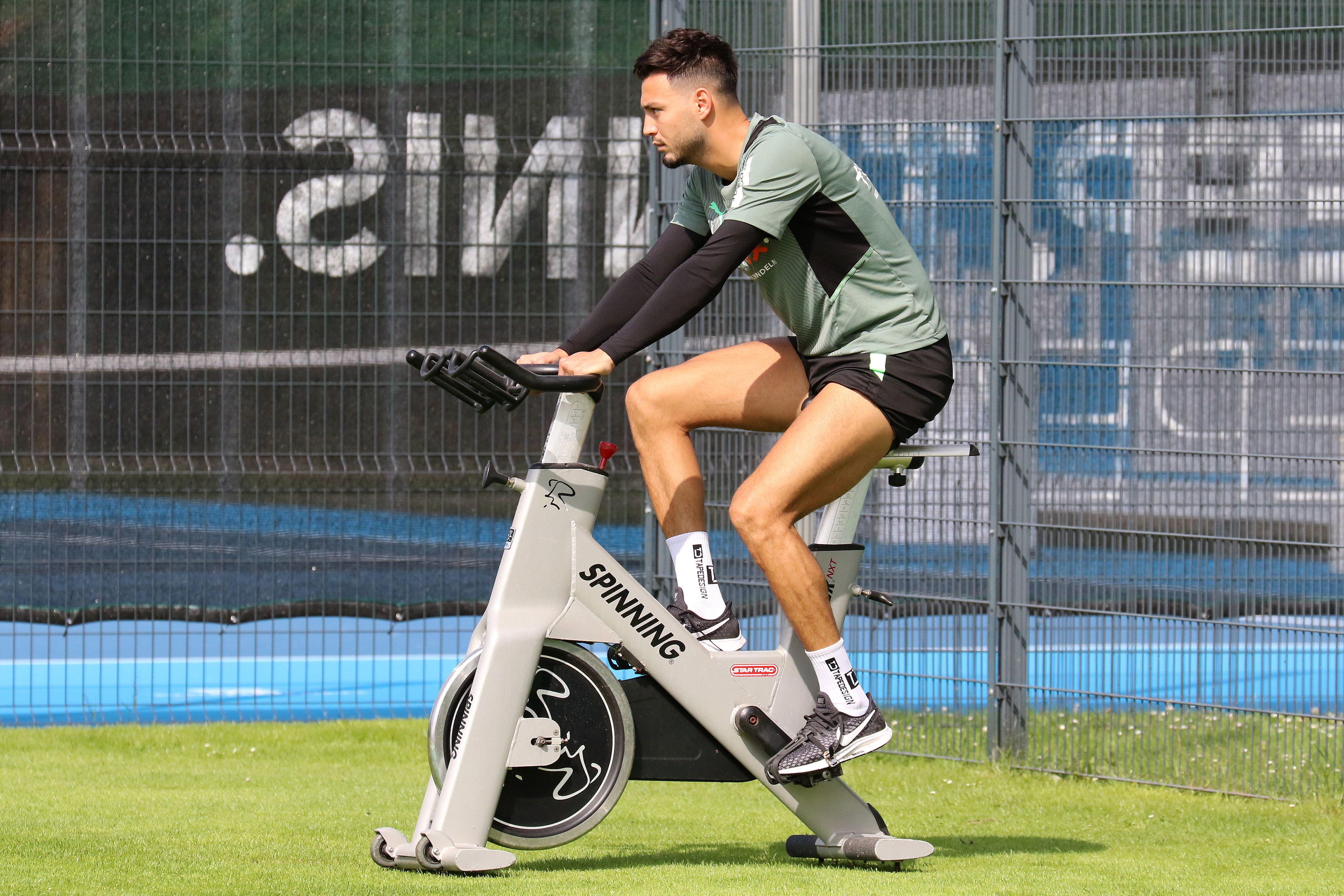 Ramy Bensebaini von Borussia Mönchengladbach sitzt am 18. Juli 2021 auf einem Spinning-Rad während des Trainingslagers in Harsewinkel. Bensebaini schaut nach vorne und radelt.